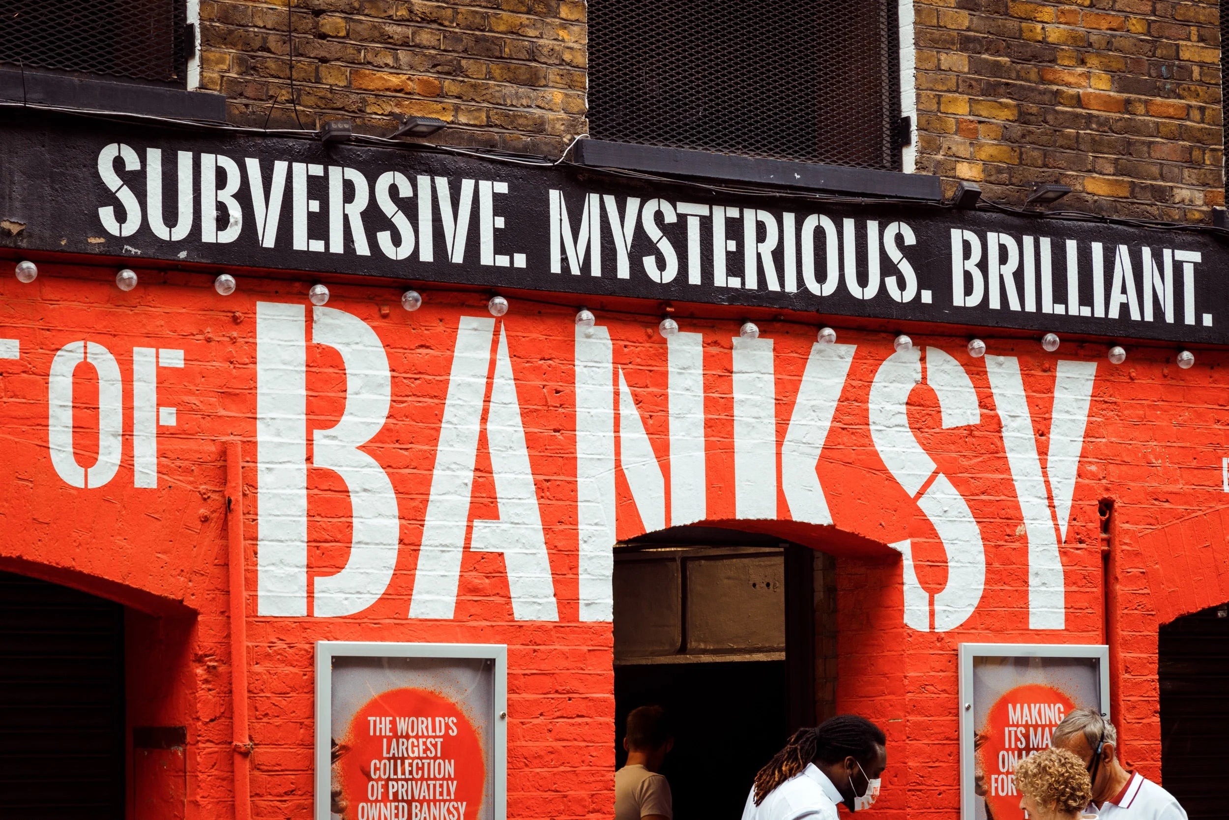 Pedestrians pass a large mural that reads "BANKSY"