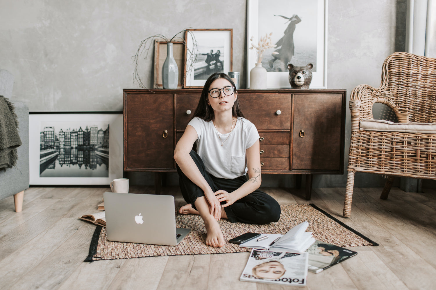 A woman sits on the floor surrounded by a laptop and papers