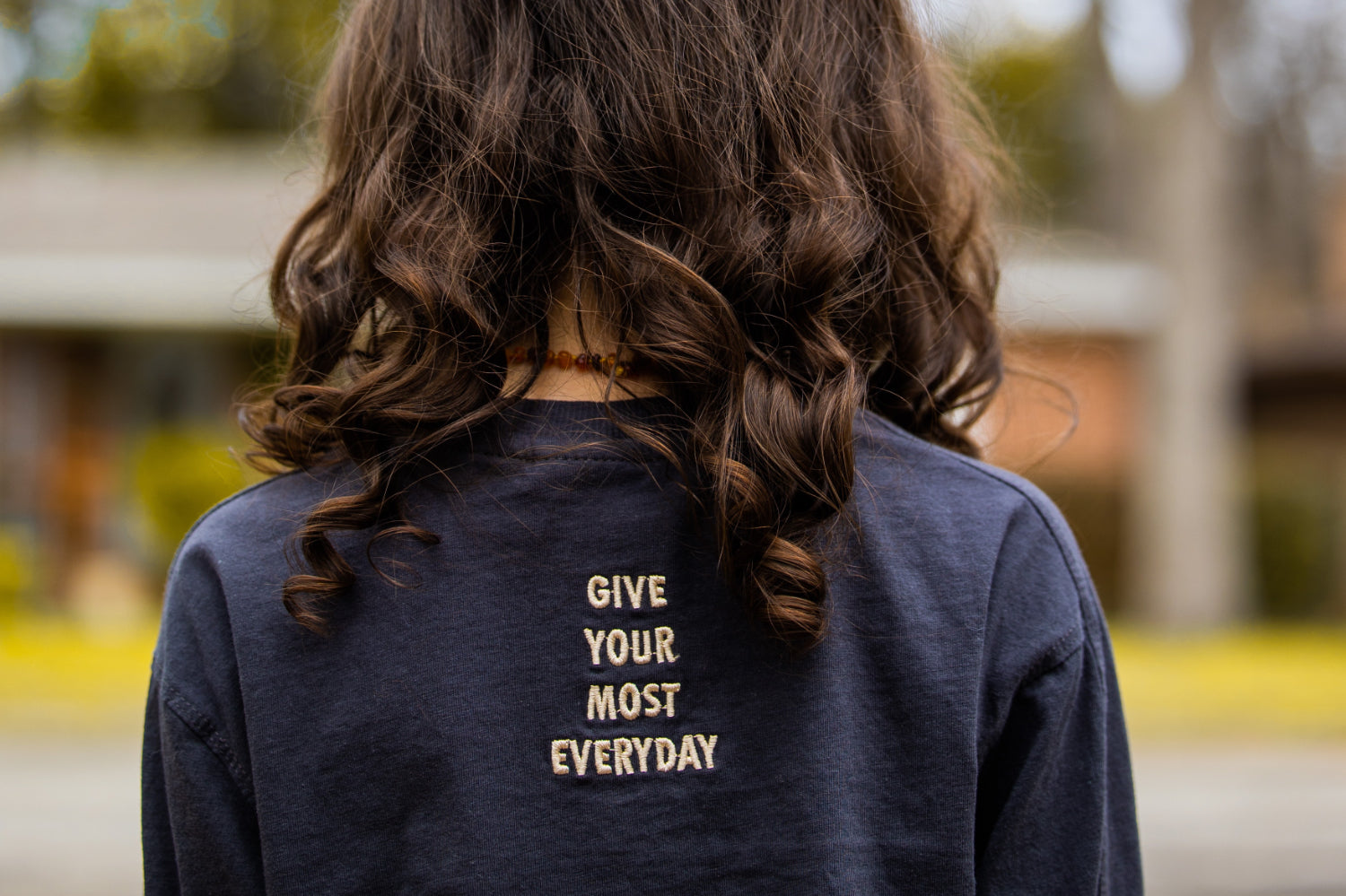 A wmen photographed from behind is wearing a shirt that reads "give our best every day"