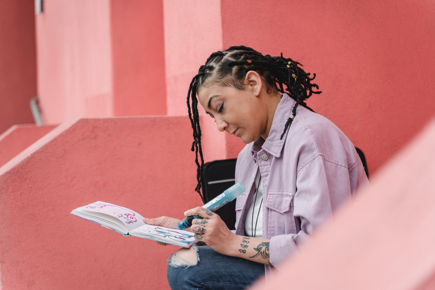 A woman sits on a set of pink stairs doodling in a notebook