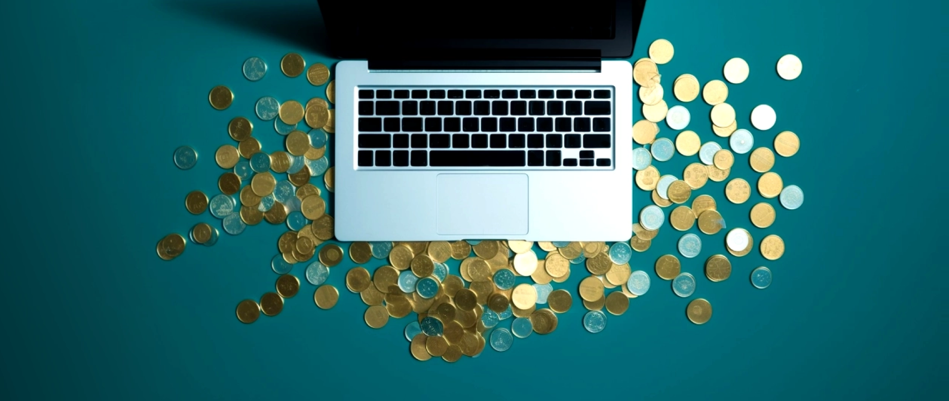 A laptop with coins around it on a blue background.