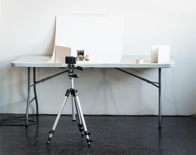 Photo of camera on tripod with product on table and white sweep in the back