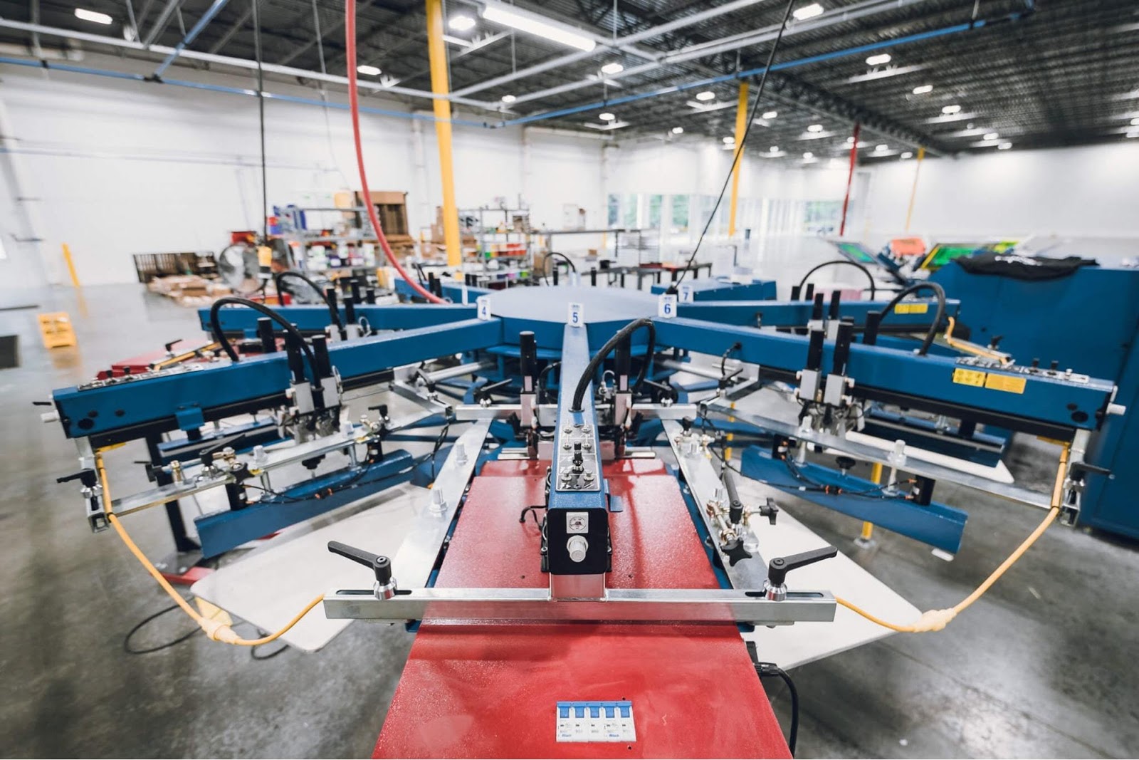 An industrial screen printing machine with eight arms in a large factory space.