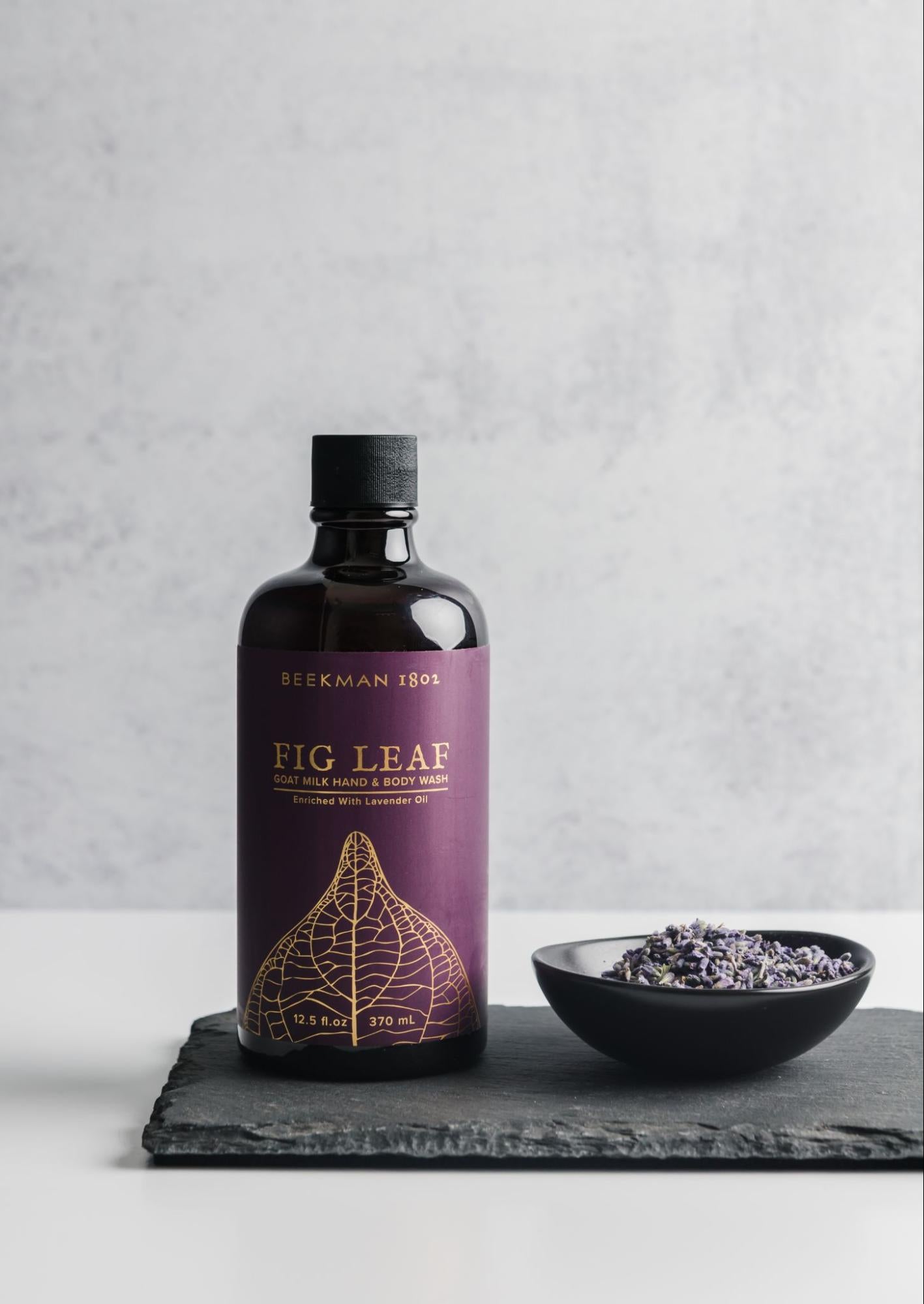 ecommerce photo of a fig-leaf body wash next to a shorter bowl of fig leaves with light source on the right casting shadows to the left