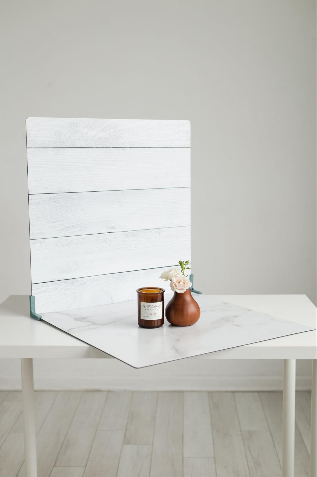 Vase with flowers and candle sitting on table with faux wood backdrop