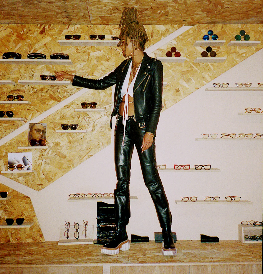 an image of the entrepreneur standing on the counter in front of a wall of sunglasses, placing a product on the shelf