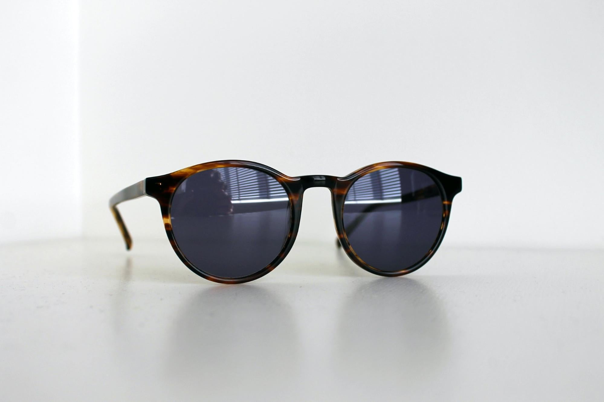 Tortoise shell sunglasses with dark lens on a white countertop with white walls in the background.