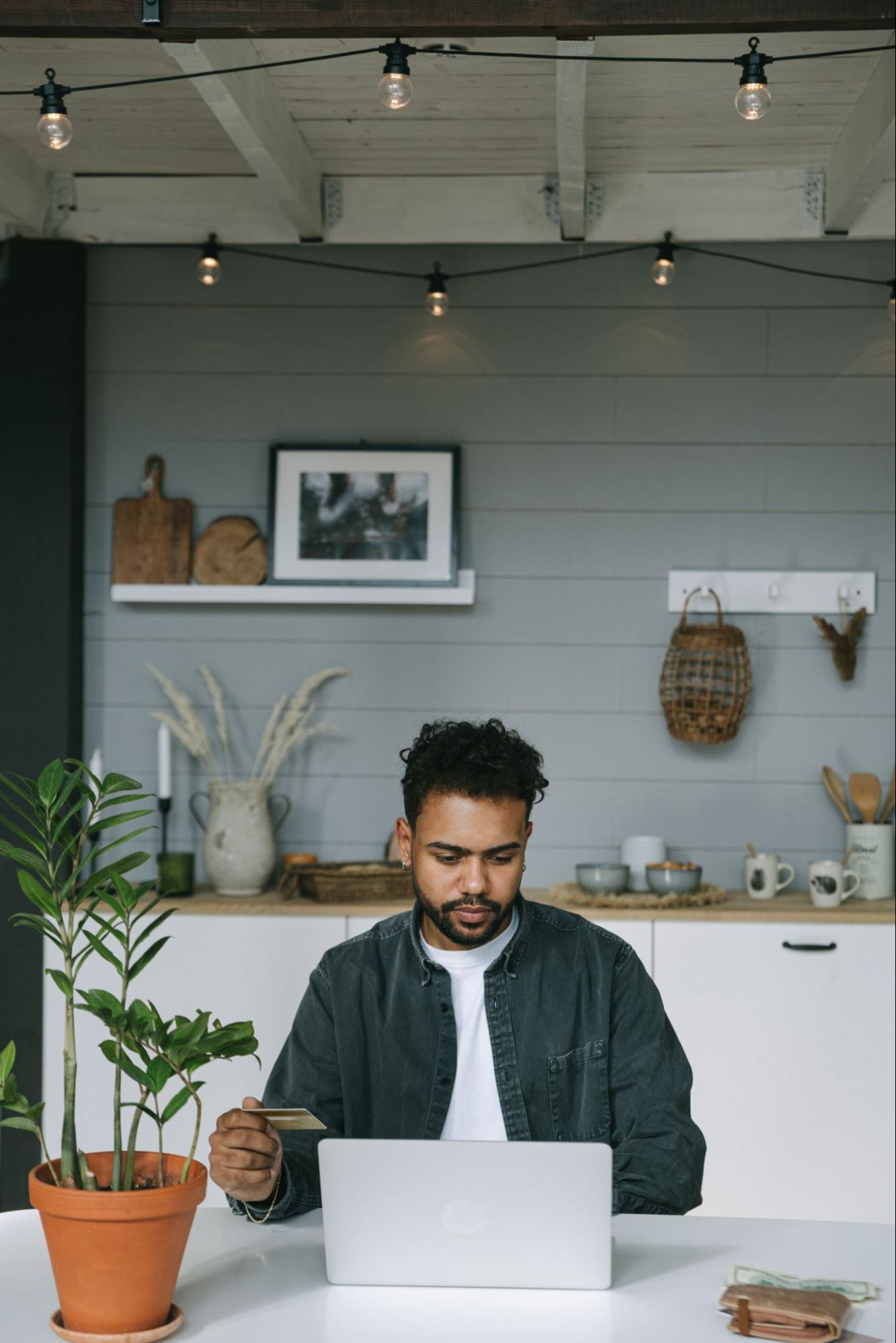 An image of a man holding up a credit card next to a laptop