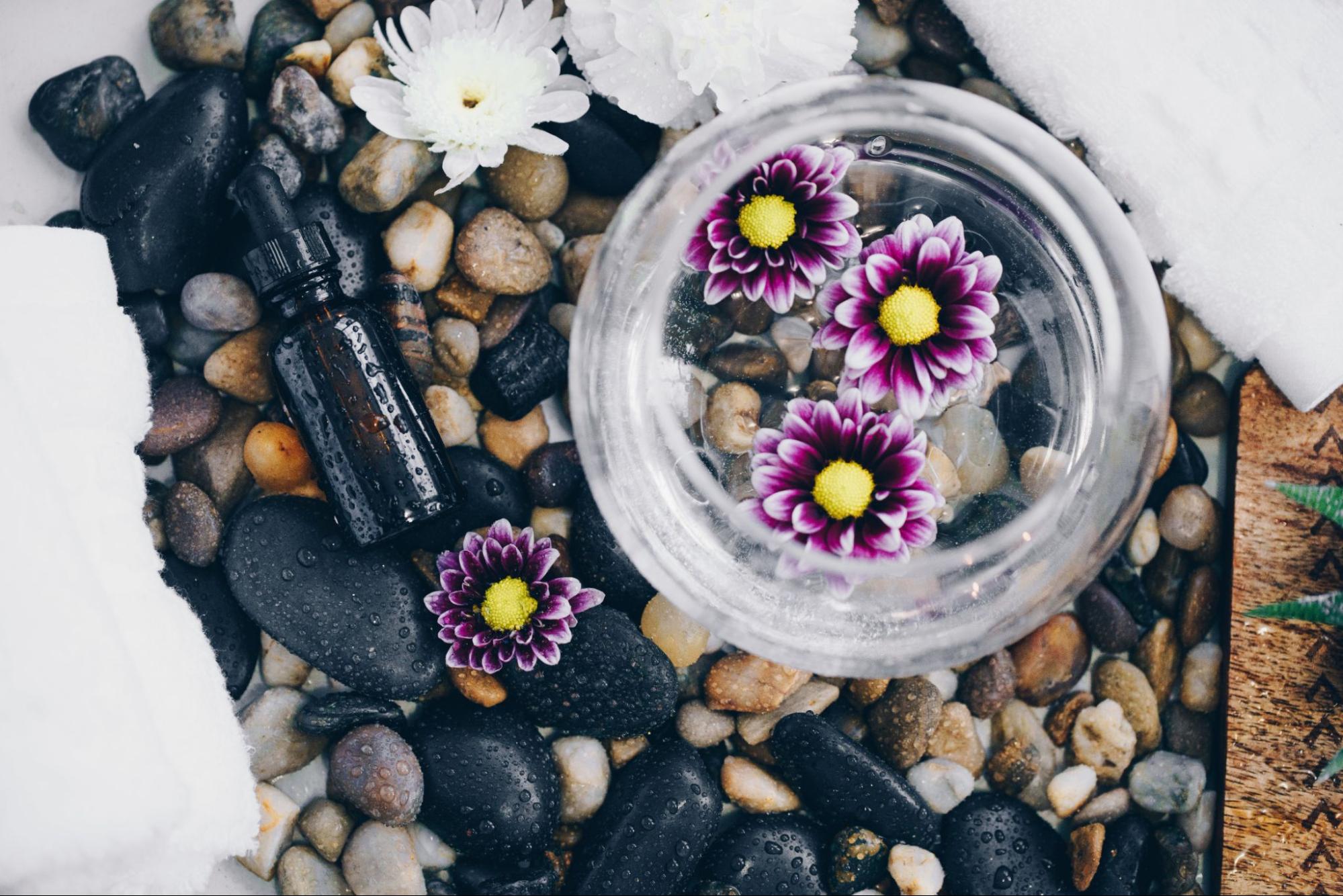 Photo of essential oil bottle among rocks and flowers