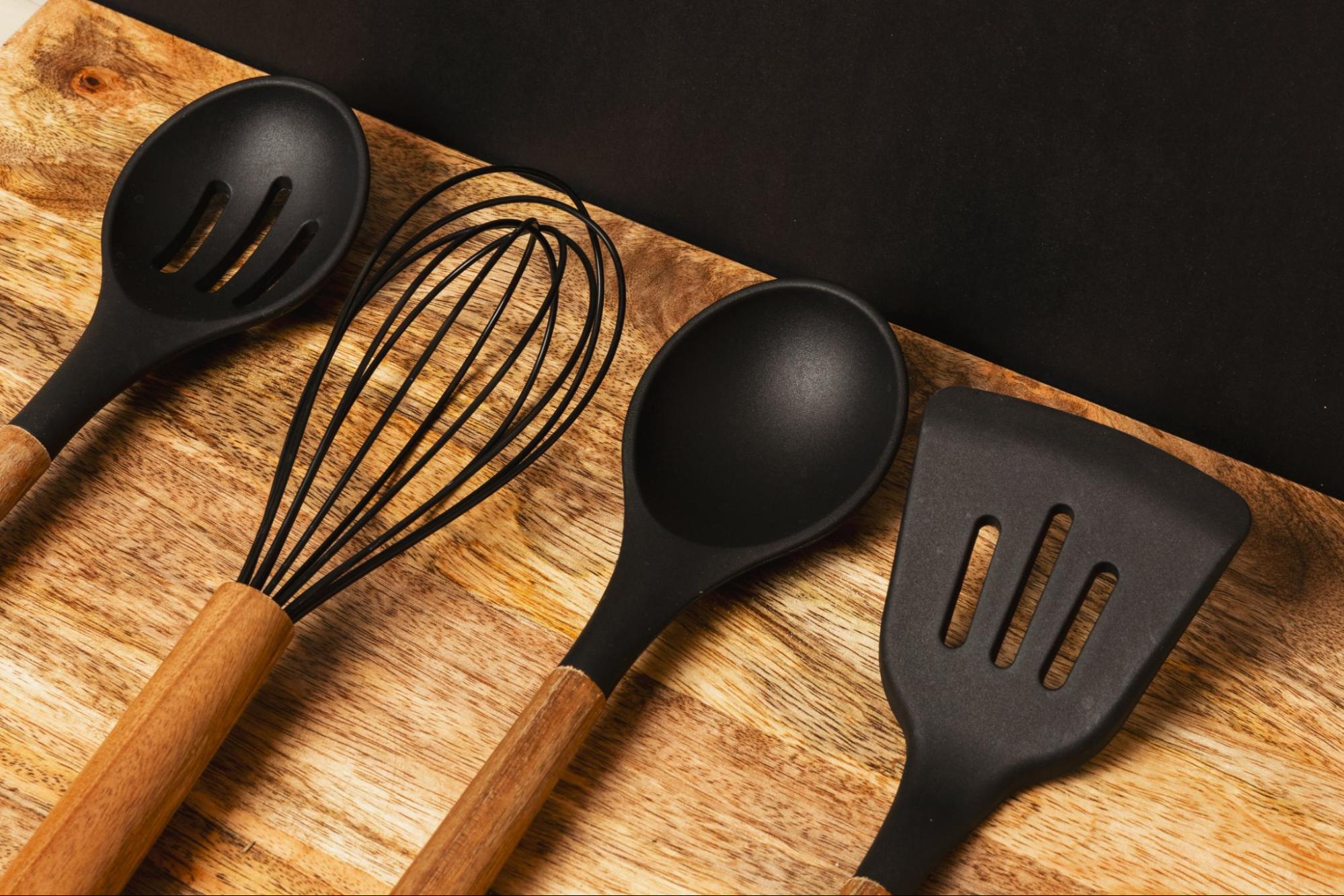 Photo of kitchenware, spoons, whisk, and spatula on a wood surface