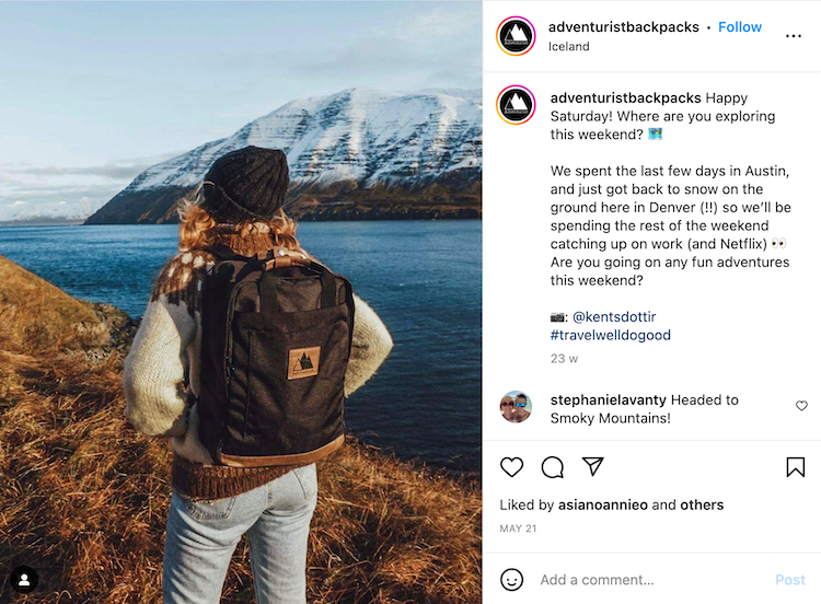 Woman with curly hair wearing a beanie hat, wool sweater, and backpack;looking at a mountain lake.