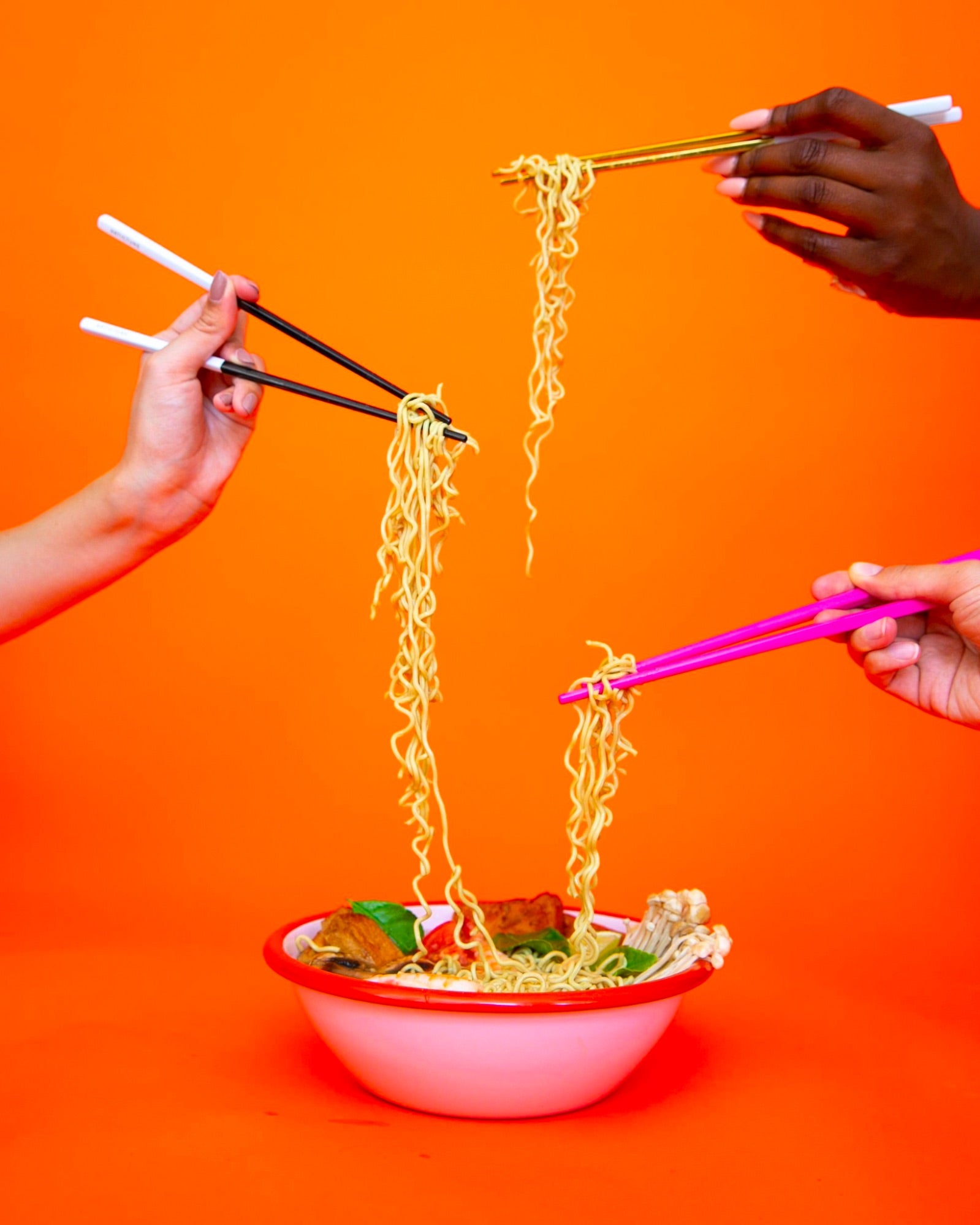 Three hands using chopsticks picking up noodles out of bowl.