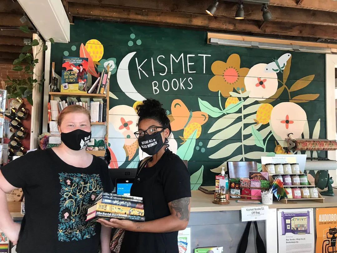 Two booksellers wearing masks pose inside a bookstore