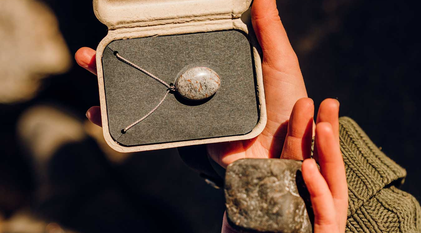 Jewelry made from a stone is presented in a box next to the stone it was made from.