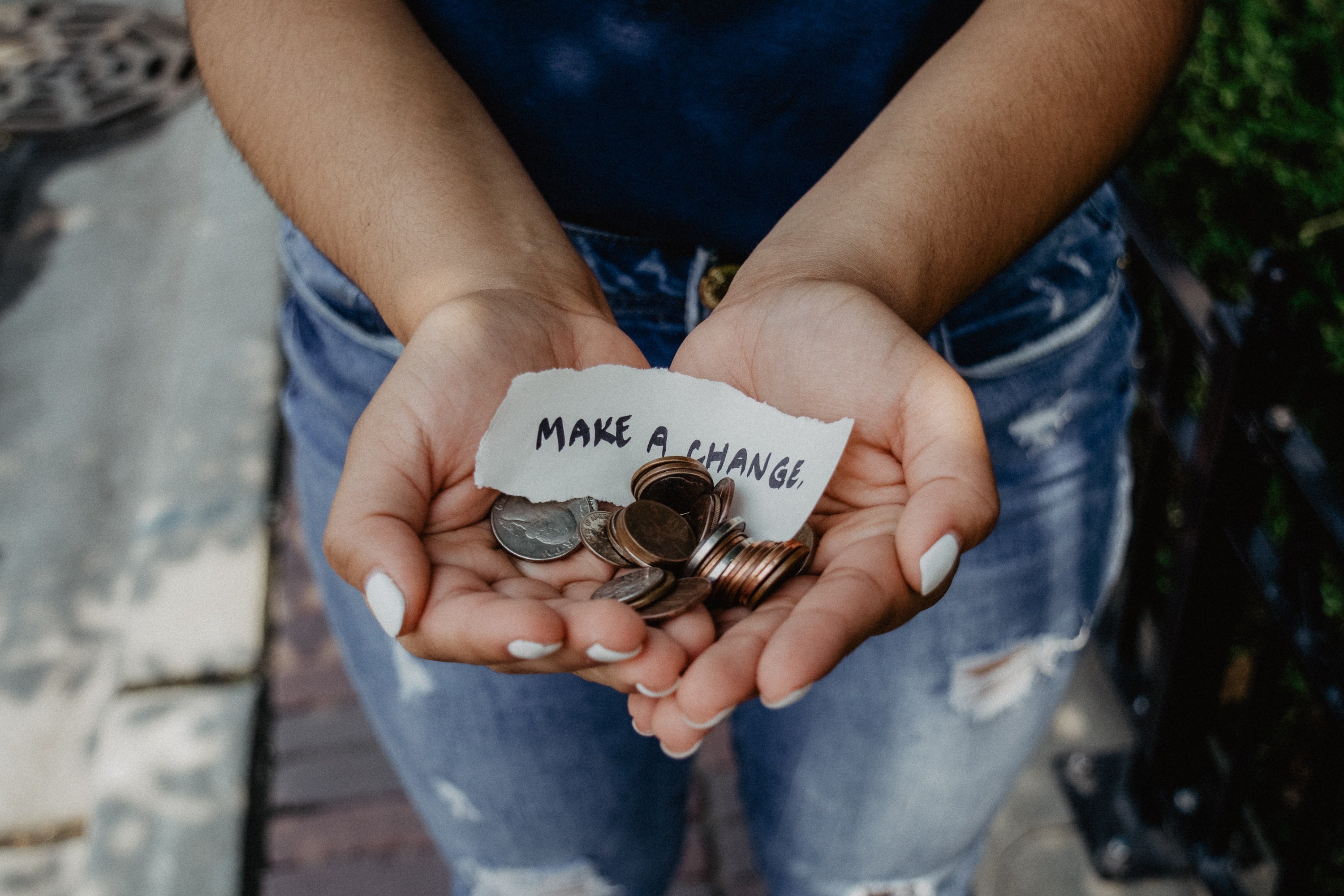 Two hands holding a piece of paper that says "make a change" and some coins. 