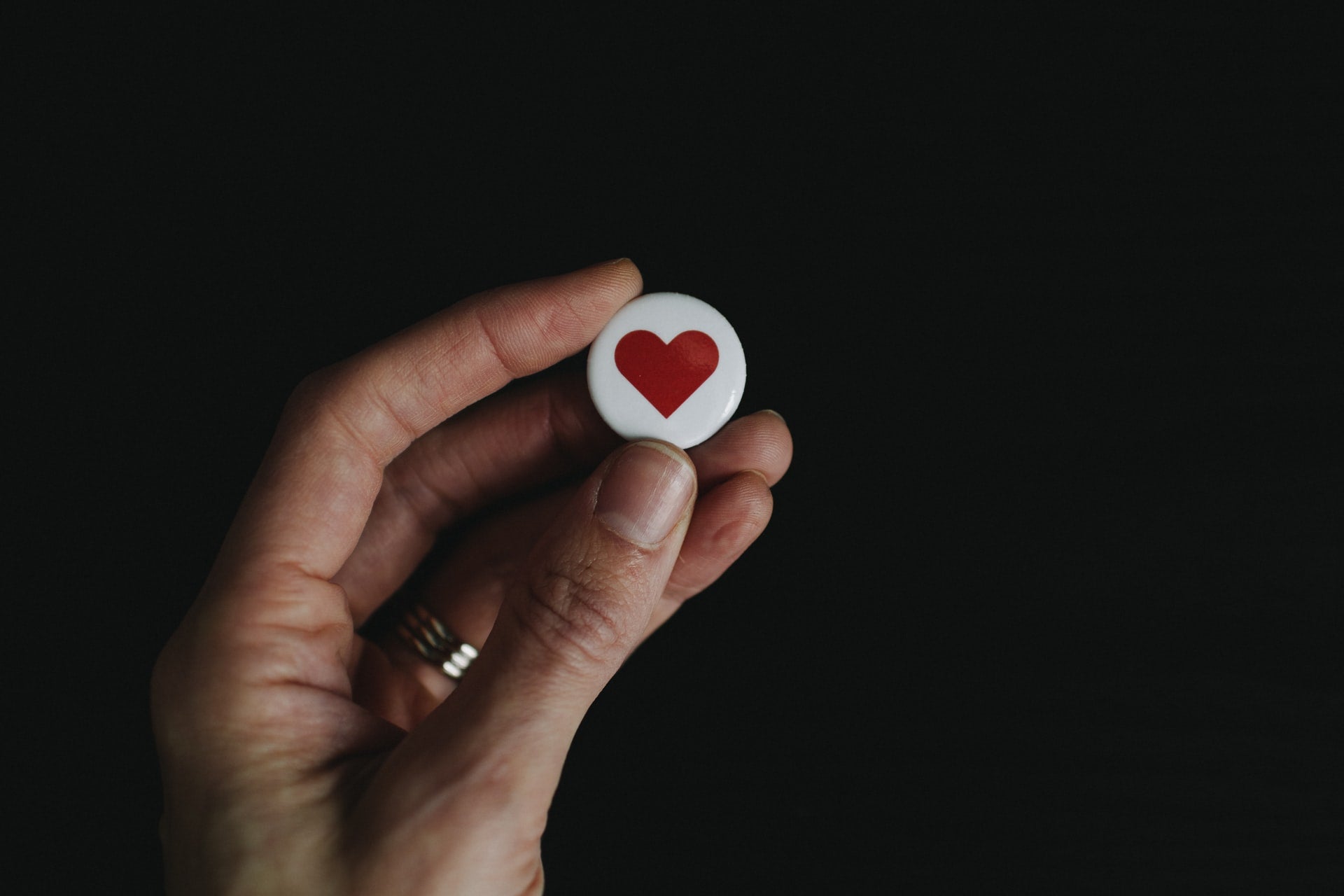 A hand holding a button with a heart representing a business trademark to be registered
