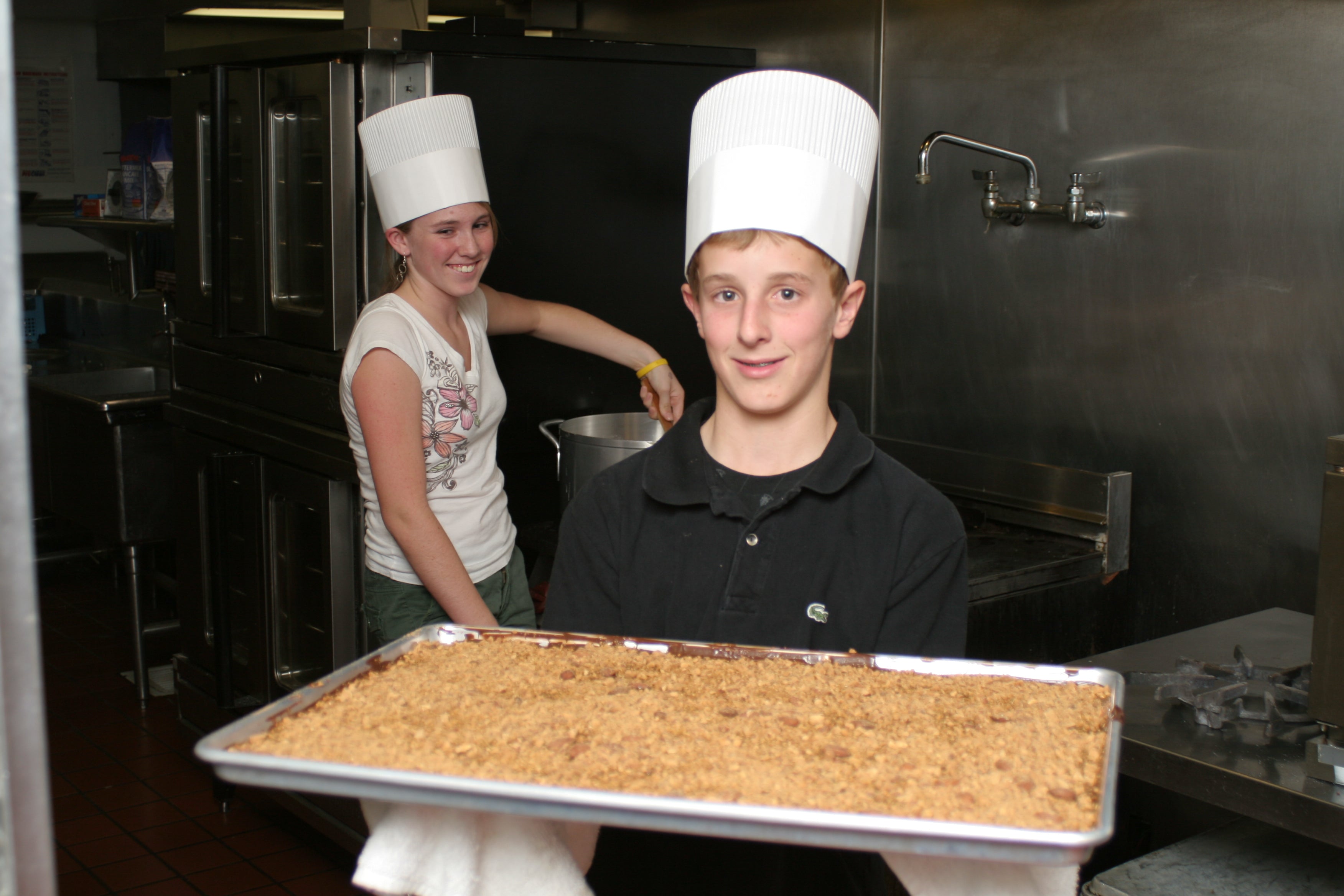 Leah Post who is on the left, stirs a pot while and Brandon Weimer on the right is displaying a tray of toffee.