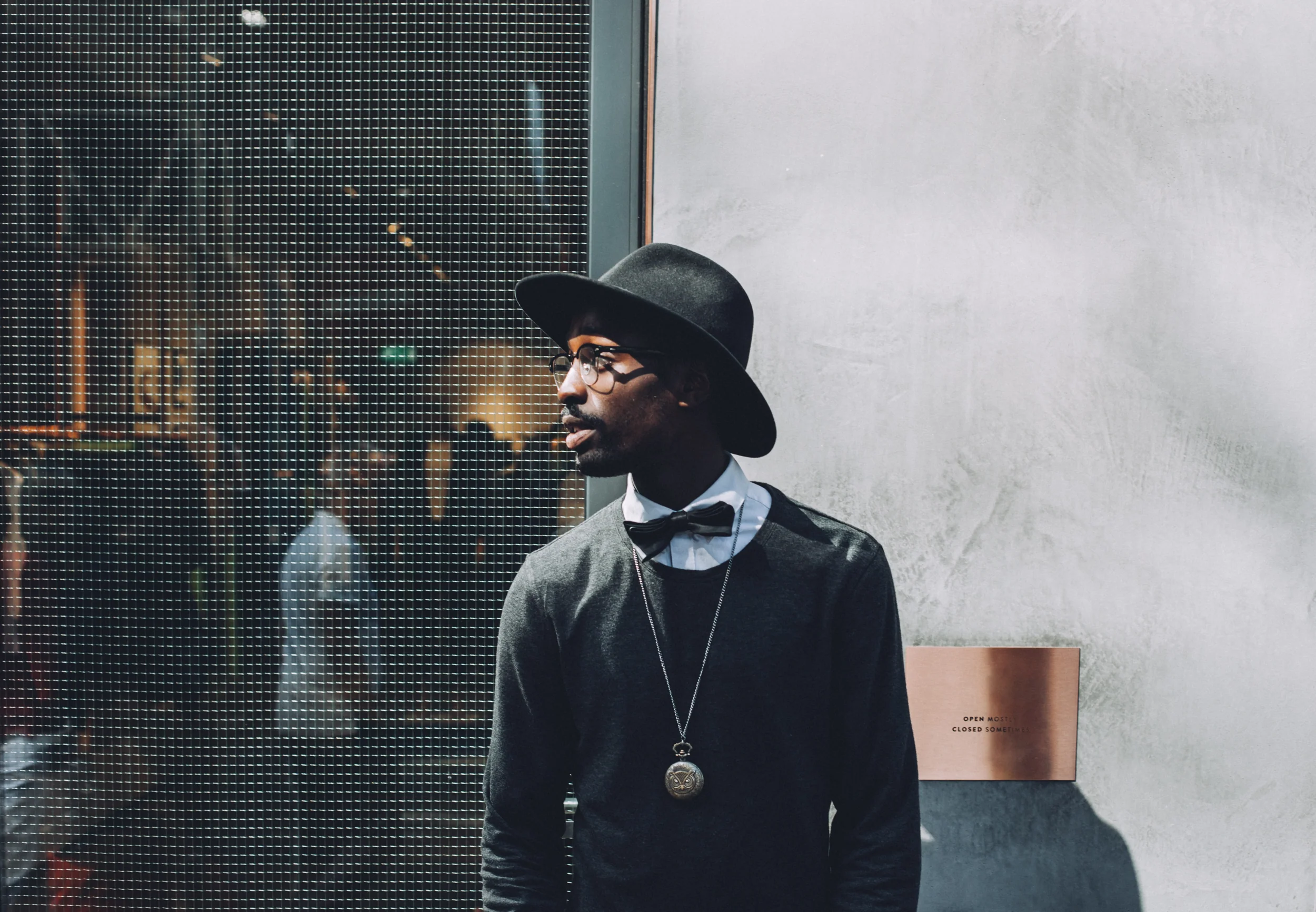 Model wearing all black poses in front of a shuttered store window