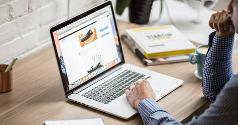 Man sitting at wood desk in bright office, reading laptop screen