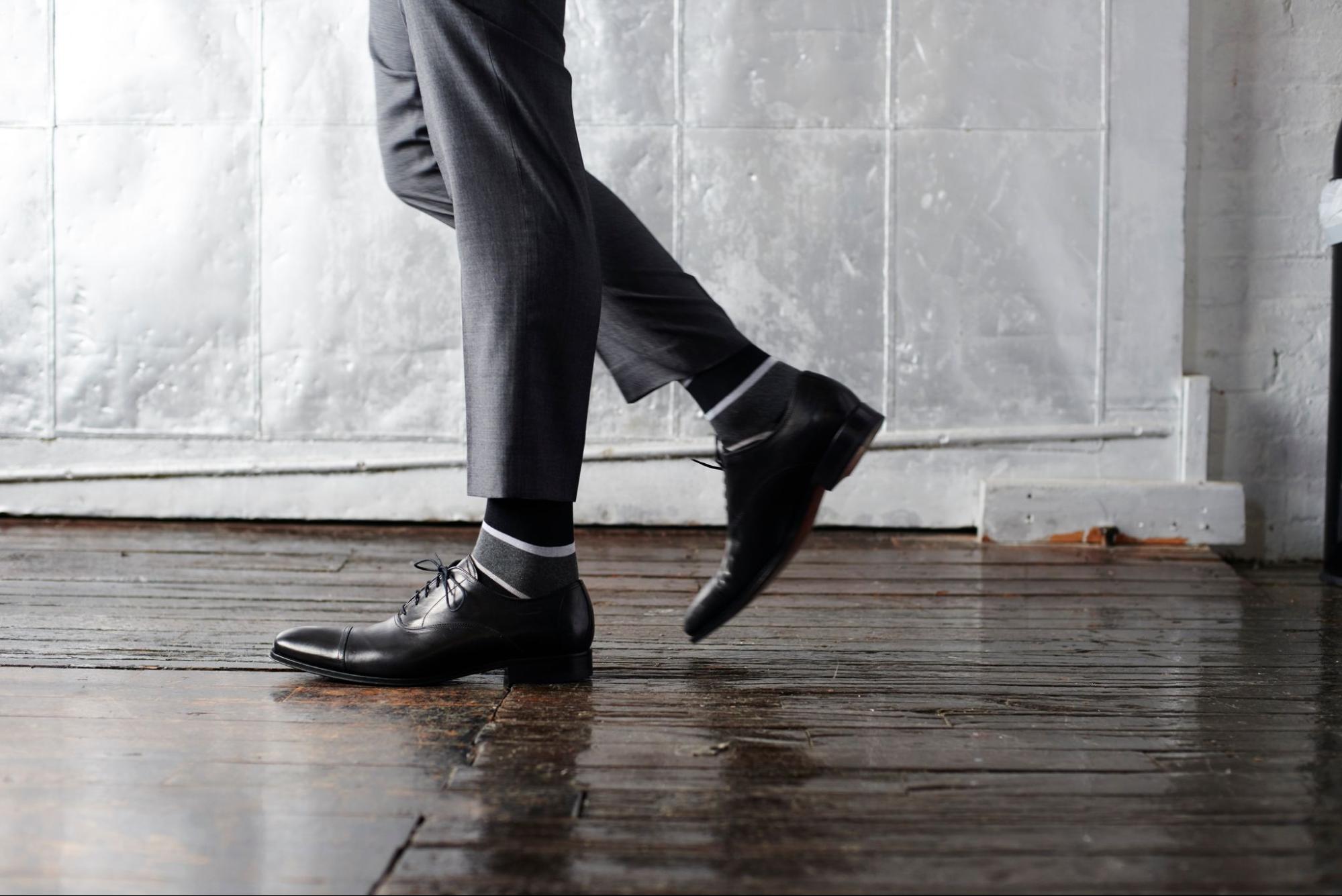 A pair of socks by Mack Weldon displayed on a model wearing leather shoes and dress pants.