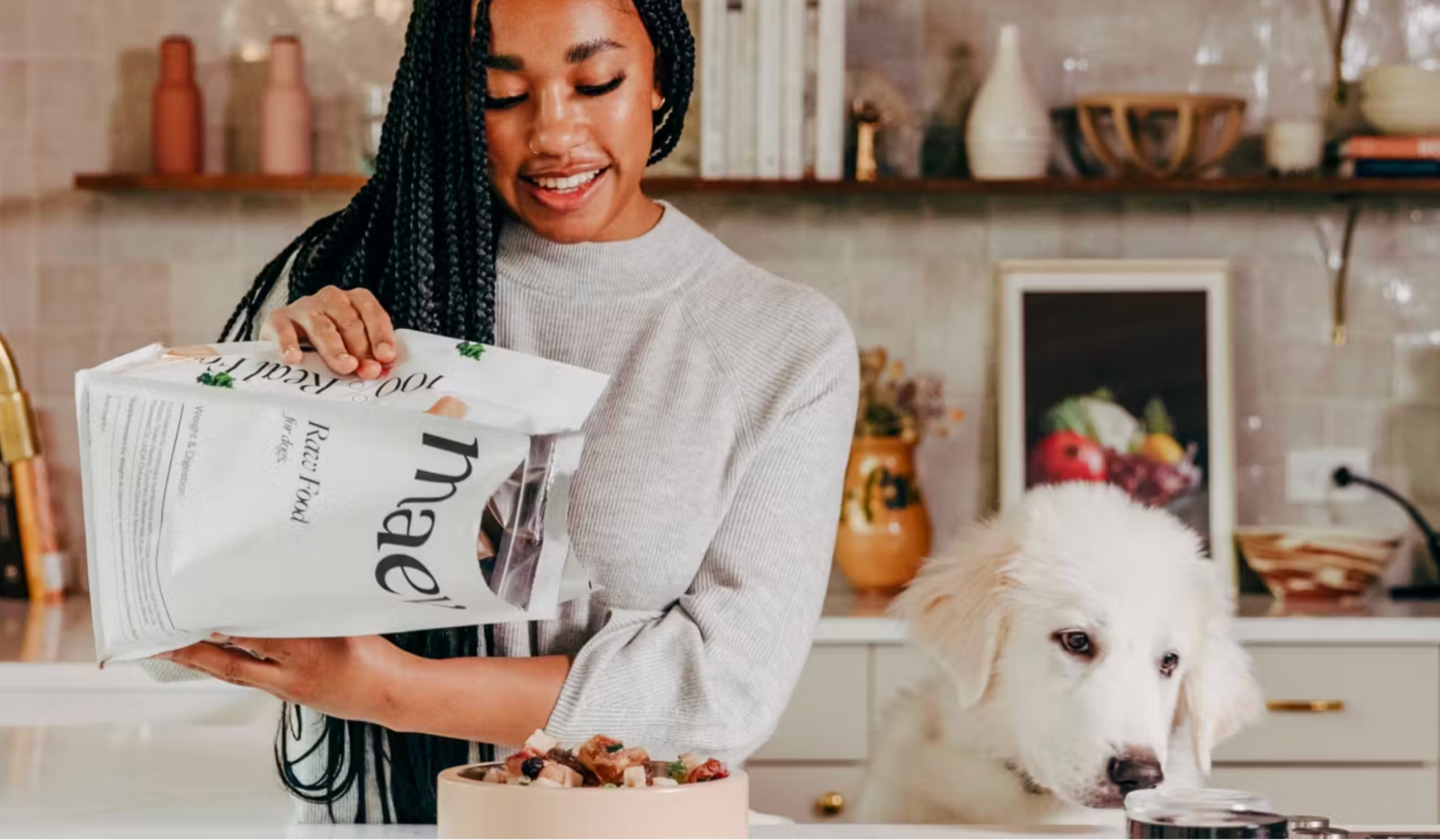 A fluffy dog waits while their owner pours Maev raw food formula into a bowl from a large bag.