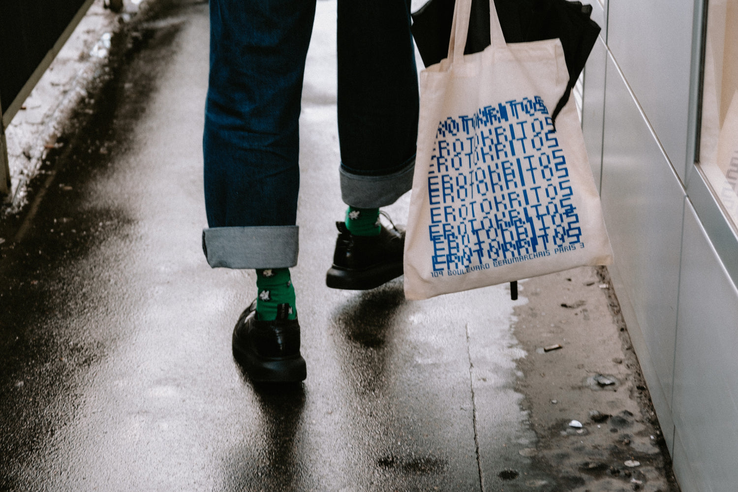 Shot of a personas legs from behind. They are carrying a graphic printed tote bag