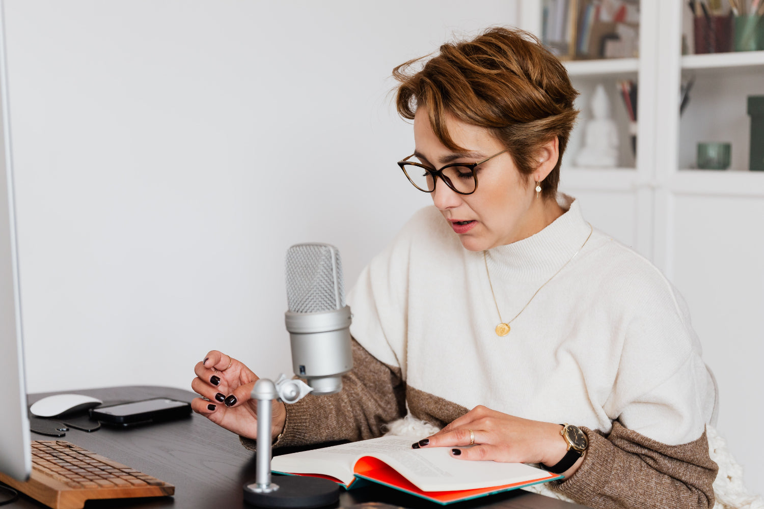 A woman speaks into a mic while reading a book