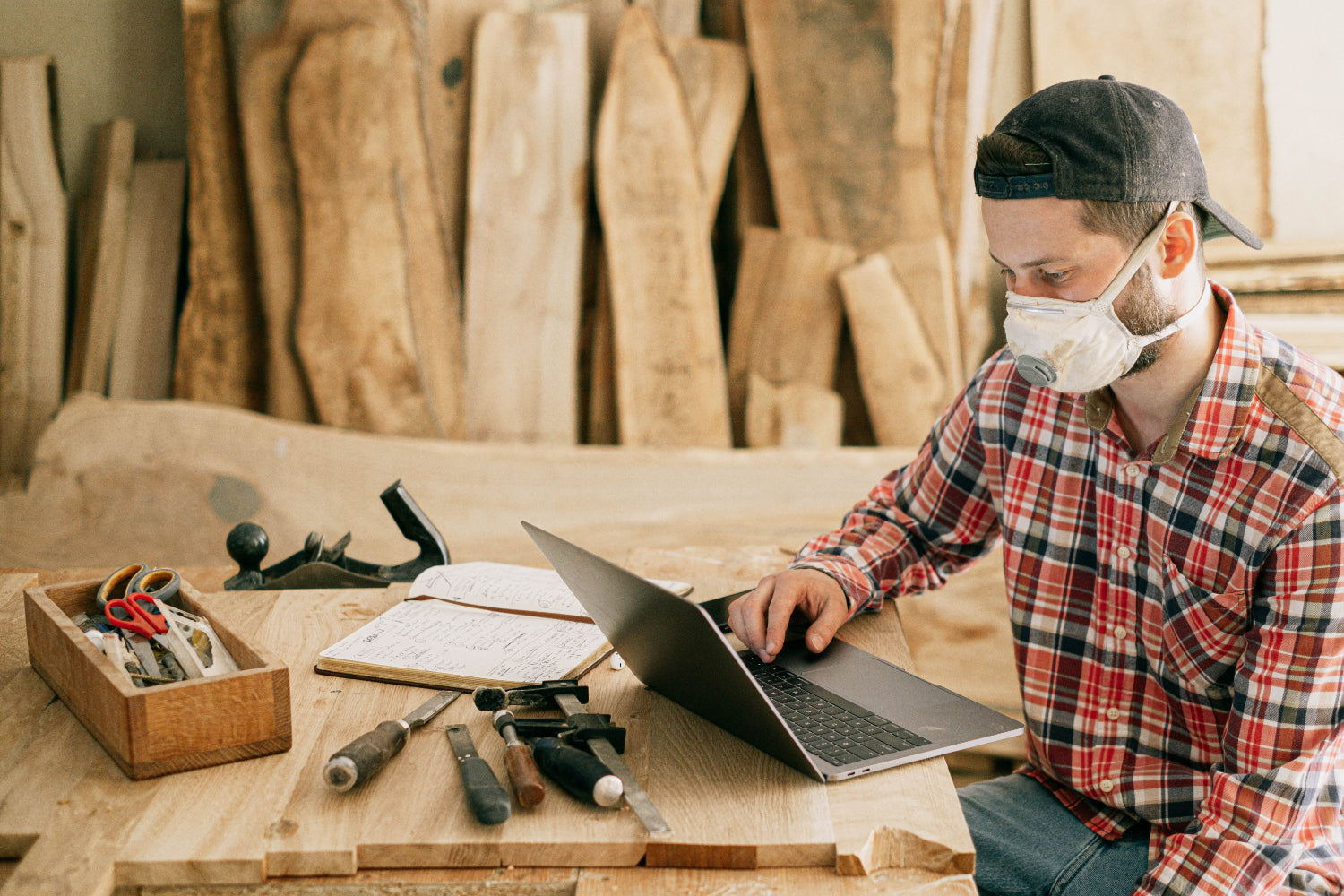 A person types on a laptop in a woodworking shop setting