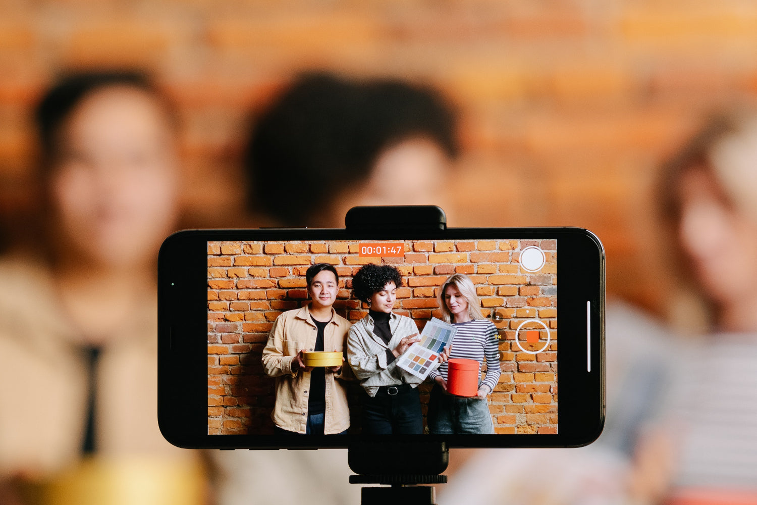 A phone captures a video of three people hanging out by a brick wall