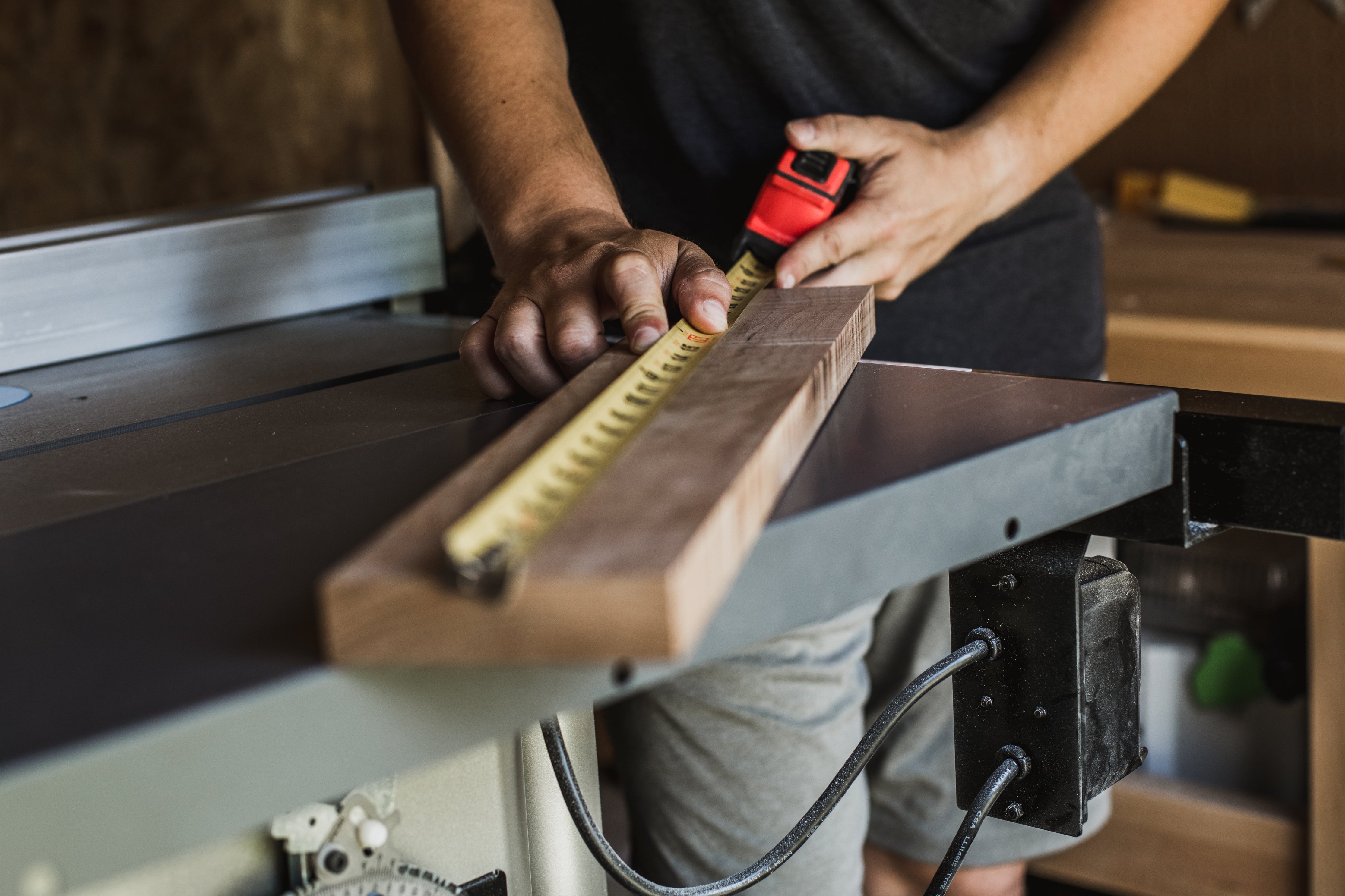 A person measures a 2x4 piece of wood in a woodworking studio