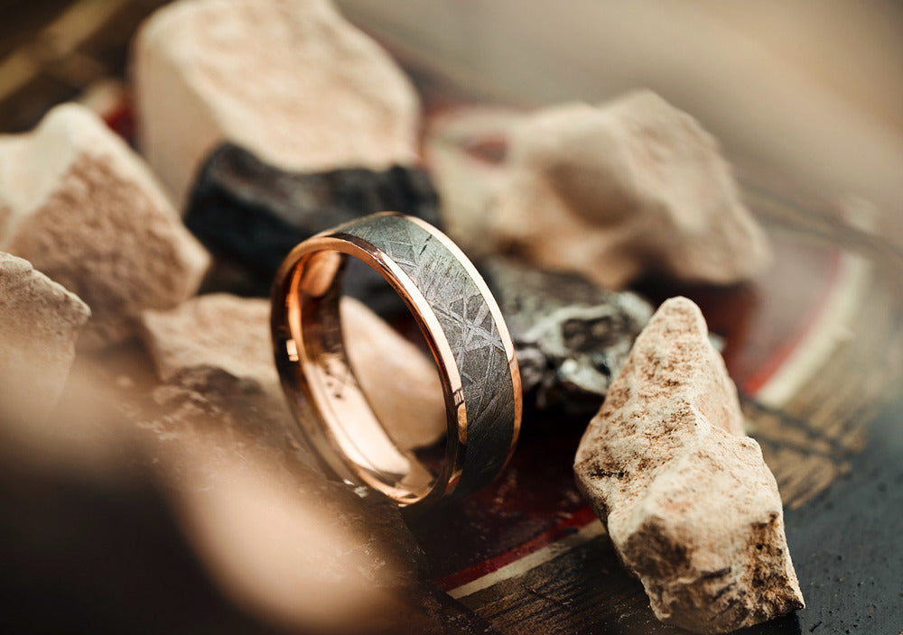 A dark ring with rose gold lining against a background filled with stones.