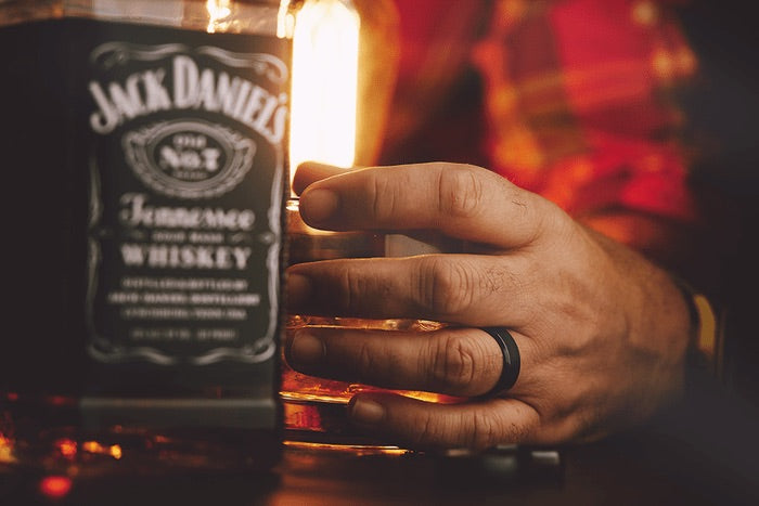 A hand model wearing a black ring reaching out to a Jack Daniels bottle. 