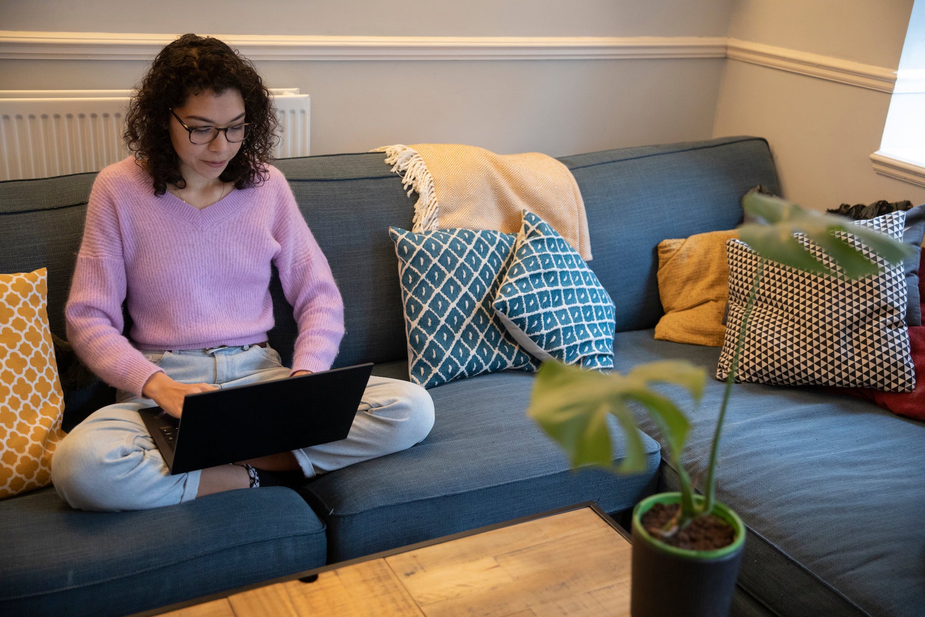 A woman sits on a blue couch typing on a laptop