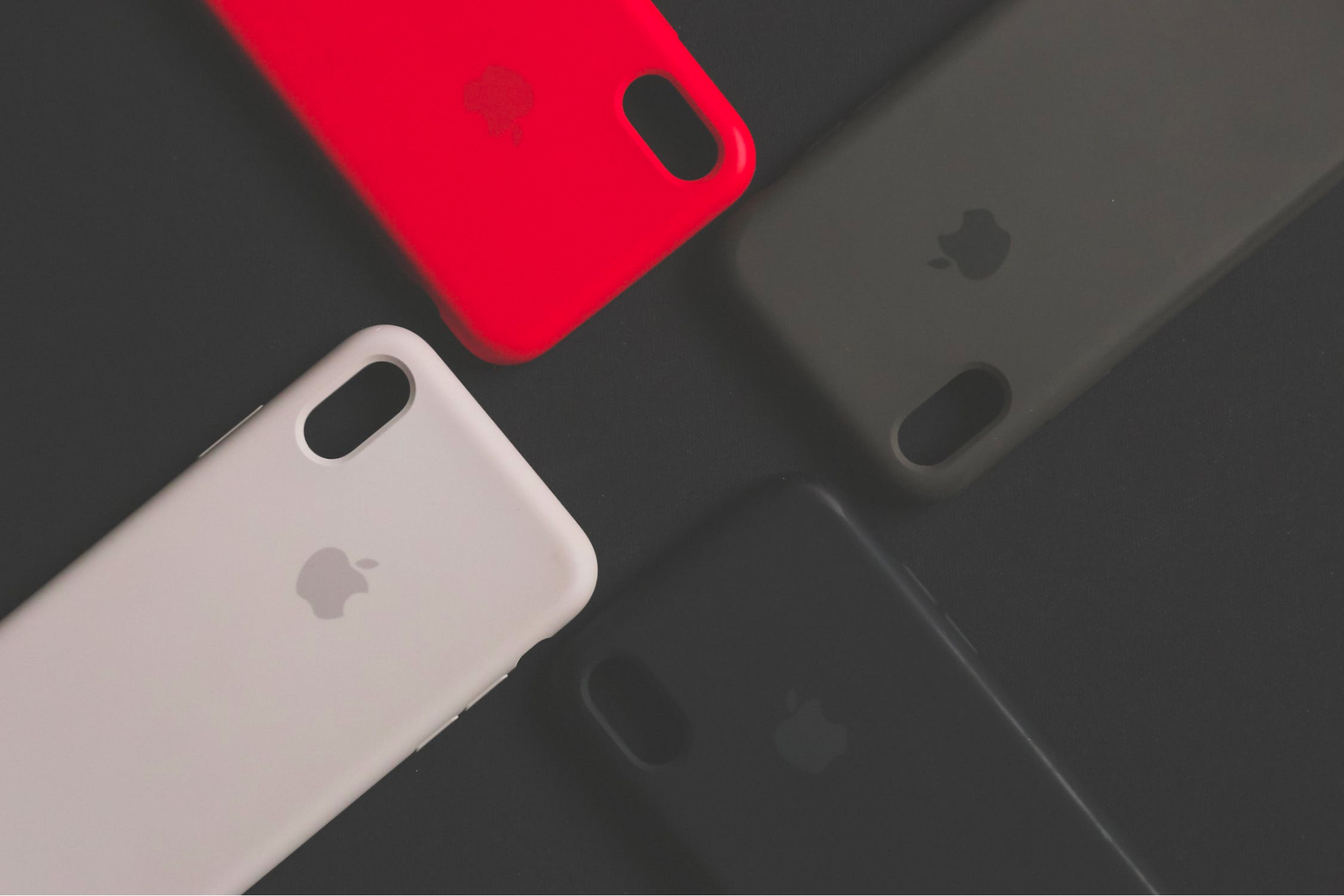 Four iPhone cases in various colors arranged on a black surface.