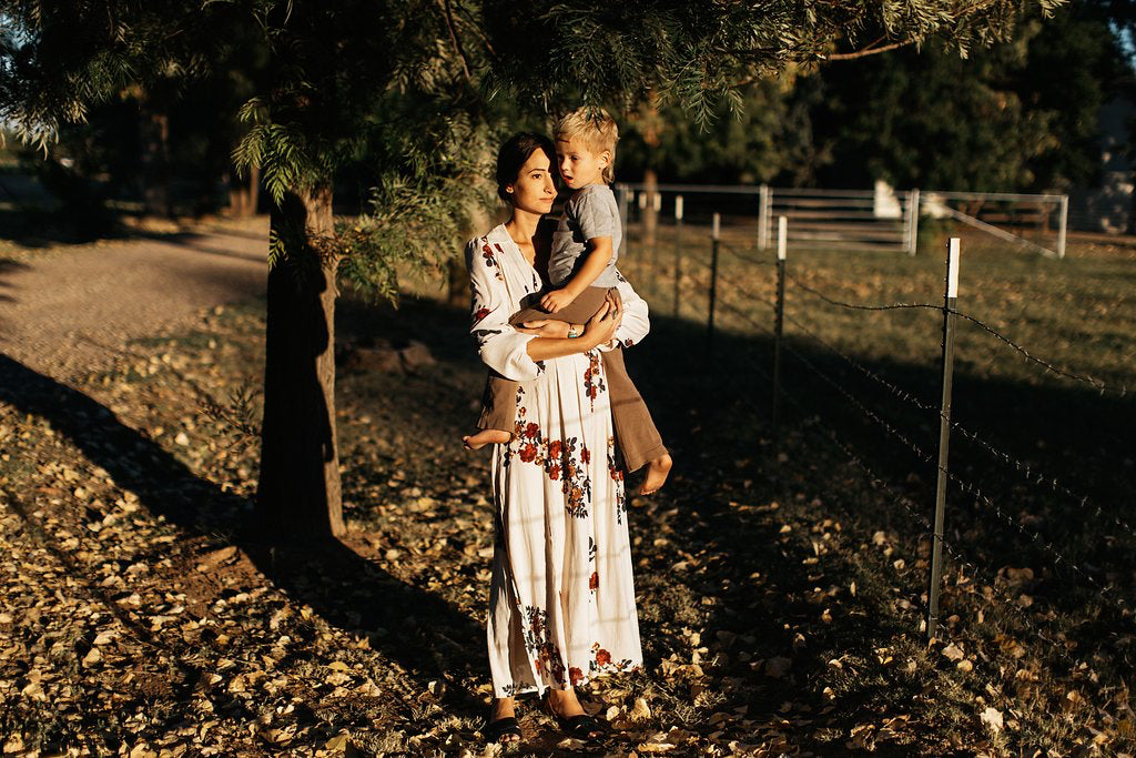 Ashley Jennet holds her child beside a fence under a tree