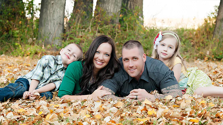 Laura Thomas and her family pose for a portrait in a pile of leaves