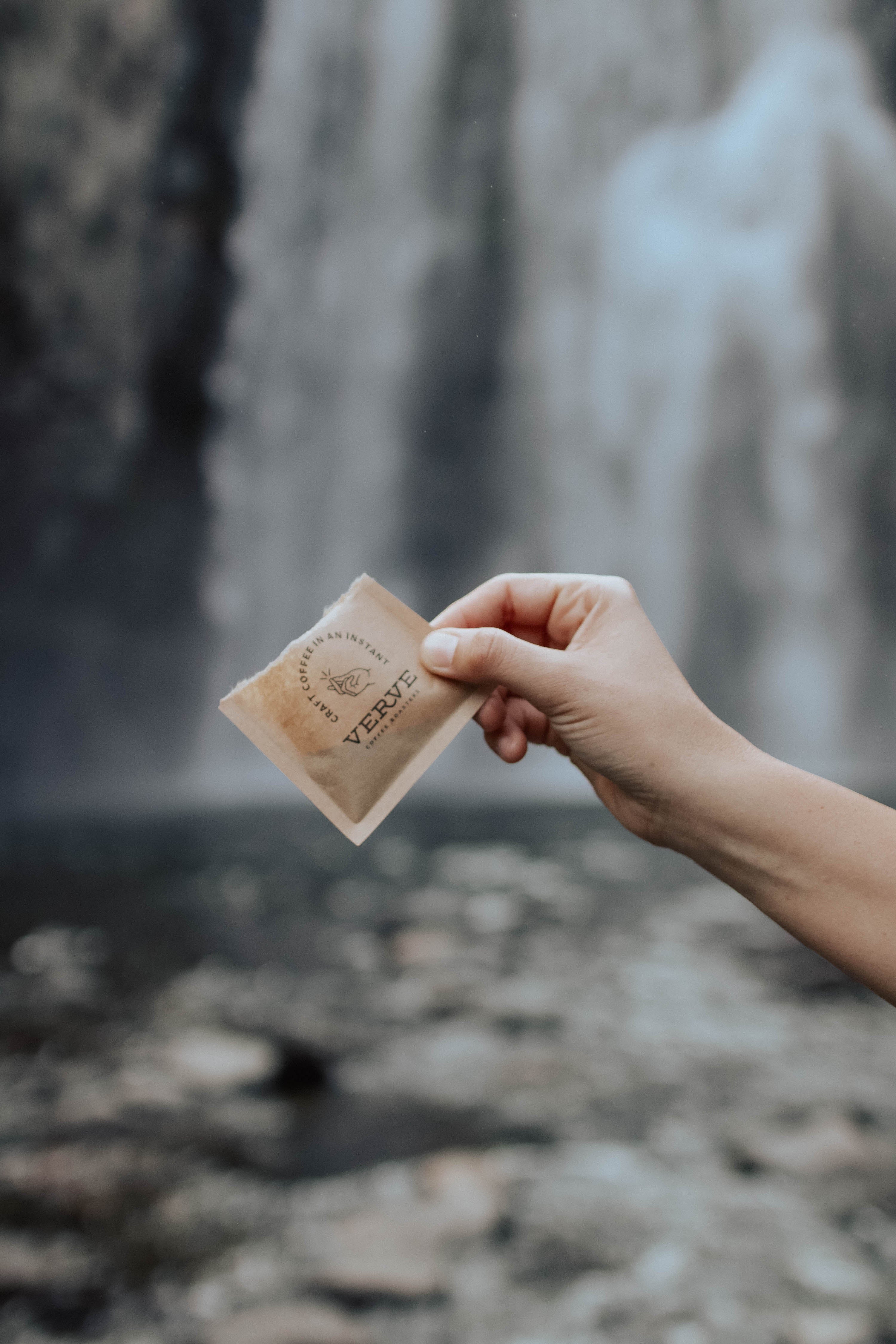 A hand holds an open bag of Verve Coffee’s craft instant blends in front of a rushing waterfall. 