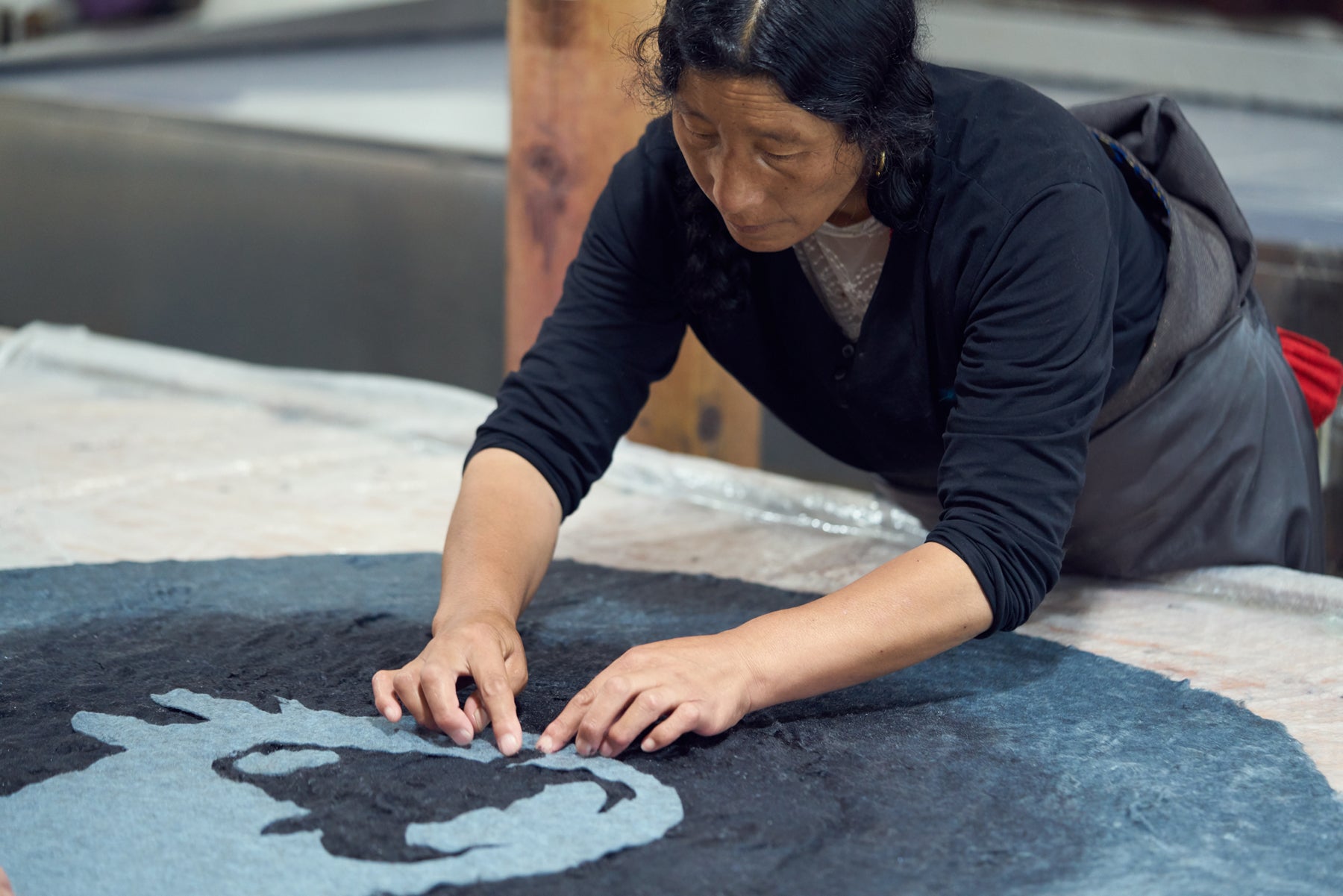 The quality control process on a piece featuring a yak imagery is being completed by an artisan in blue shirt and grey pants. 