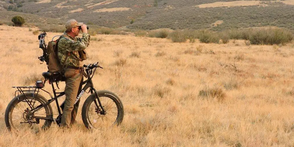A man on an off-road ebike surveys a dry meadow with a pair of binoculars.