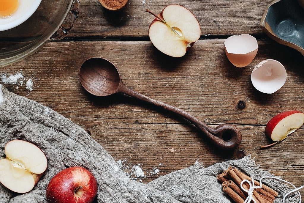 Handcrafted wooden spoon laying on a wooden table with cut apples