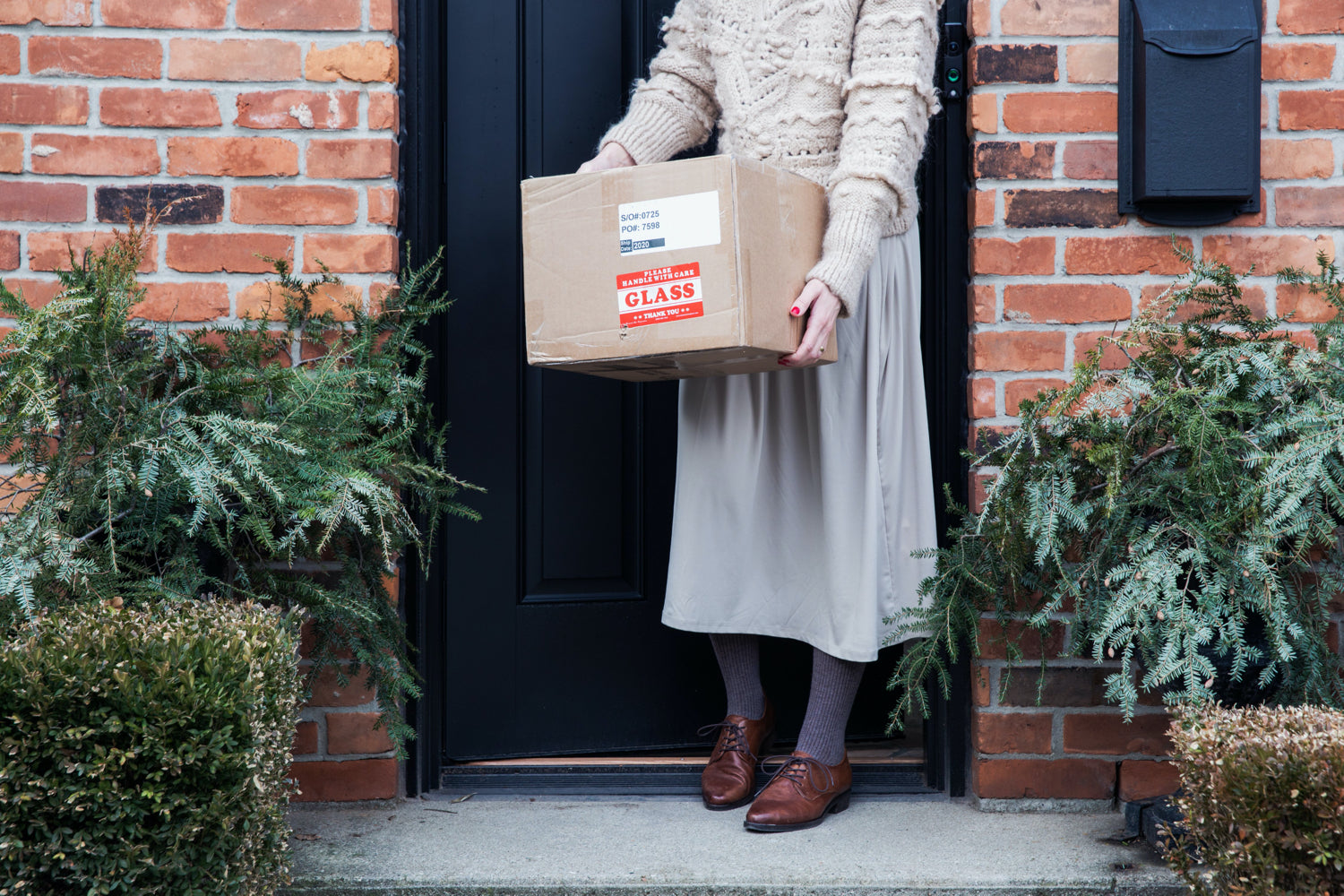 Una donna tiene una scatola di cartone sul gradino davanti alla porta di casa