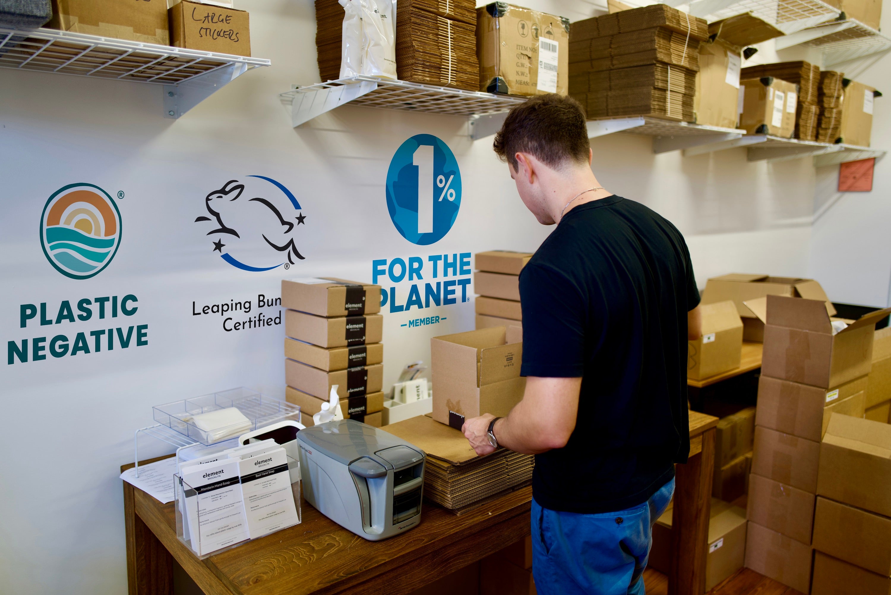 A picking and packing station including a shipping label printer, packed boxes and a fulfillment worker.