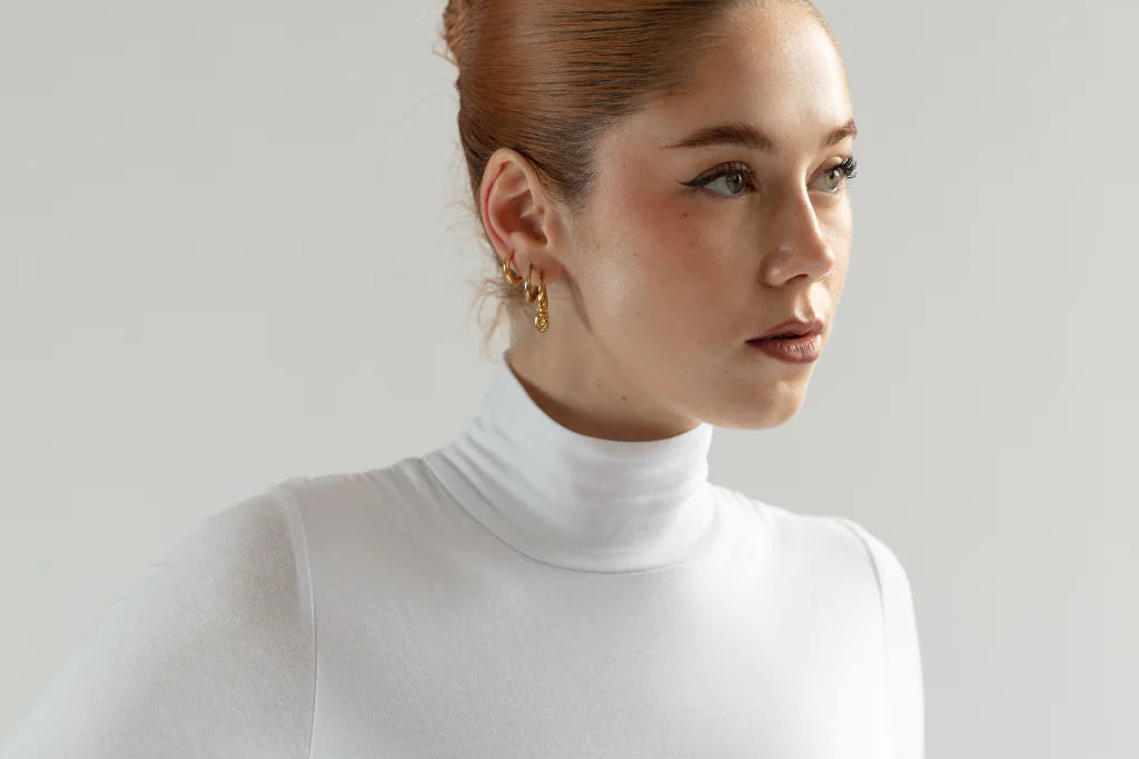 A woman models a tight white cotton turtleneck top