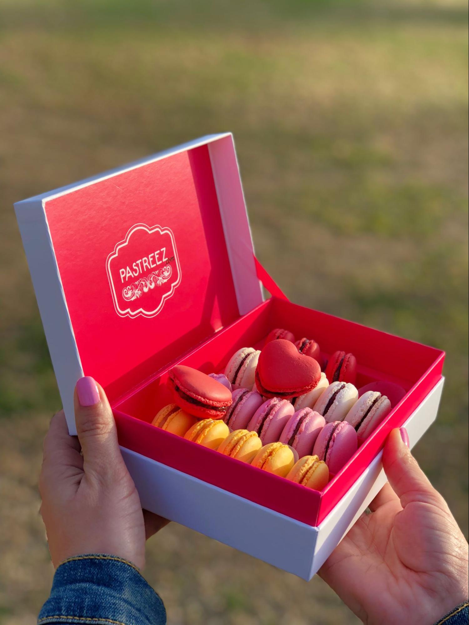 A box of heart shaped macarons by Pastreez held by a hand model.