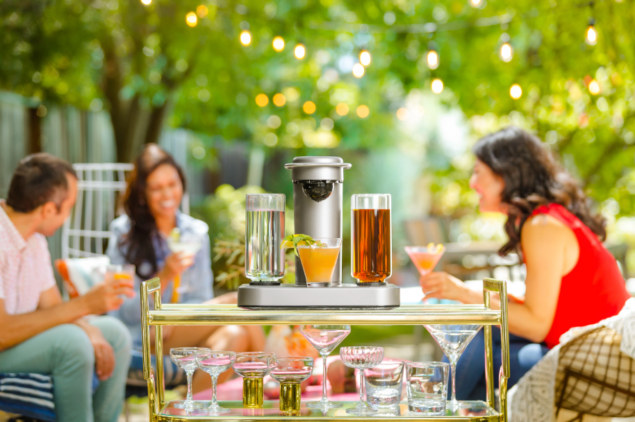 Image of the Bartesian on a bar cart with people drinking cocktails in the background