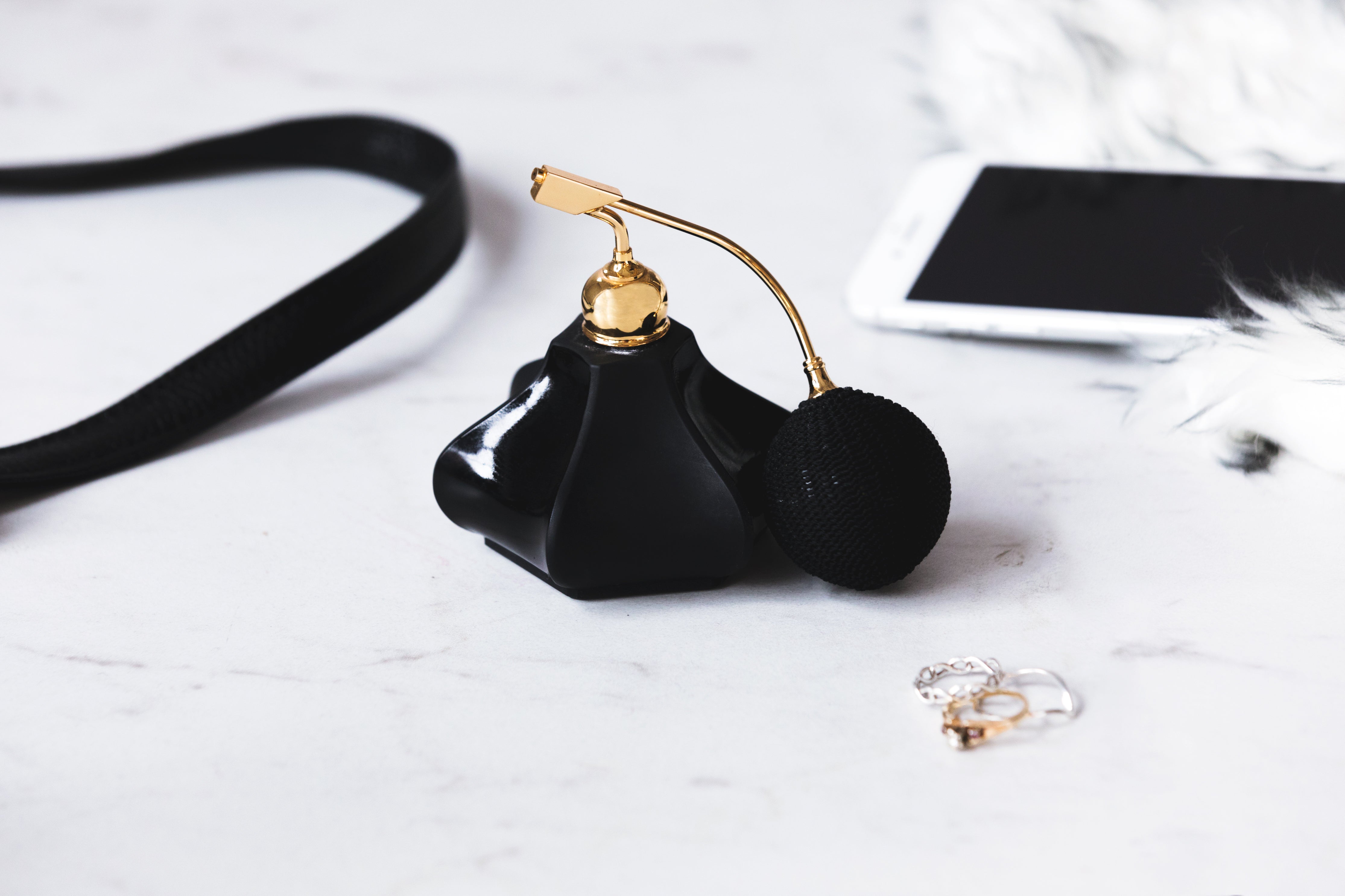 A black glass perfume bottle sits on a marble surface