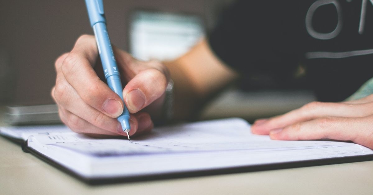 A hand holding a blue pen writing in a notebook