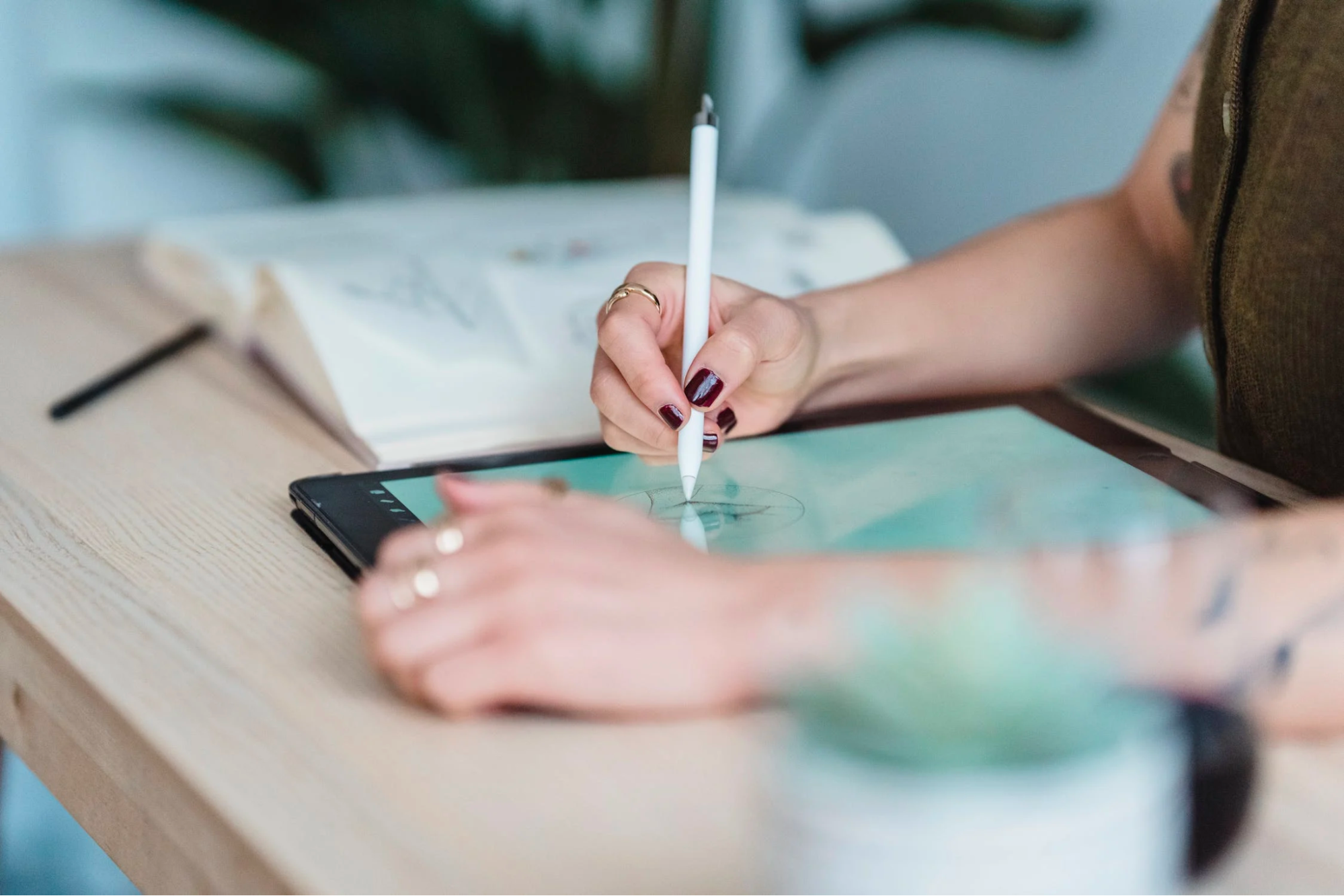 A digital artist wearing rings and sitting at a desk, drawing on a tablet.