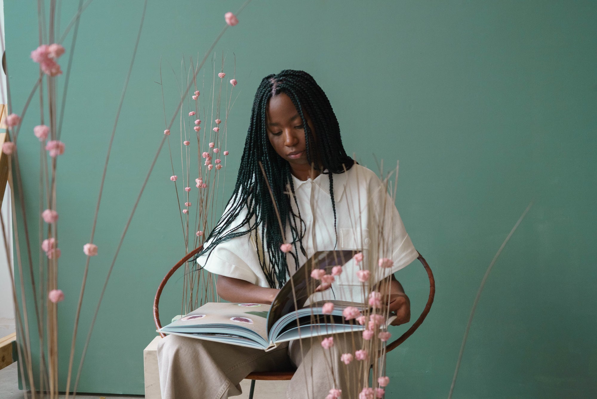 A person reads a book and sits on a chair surrounded by pink foliage