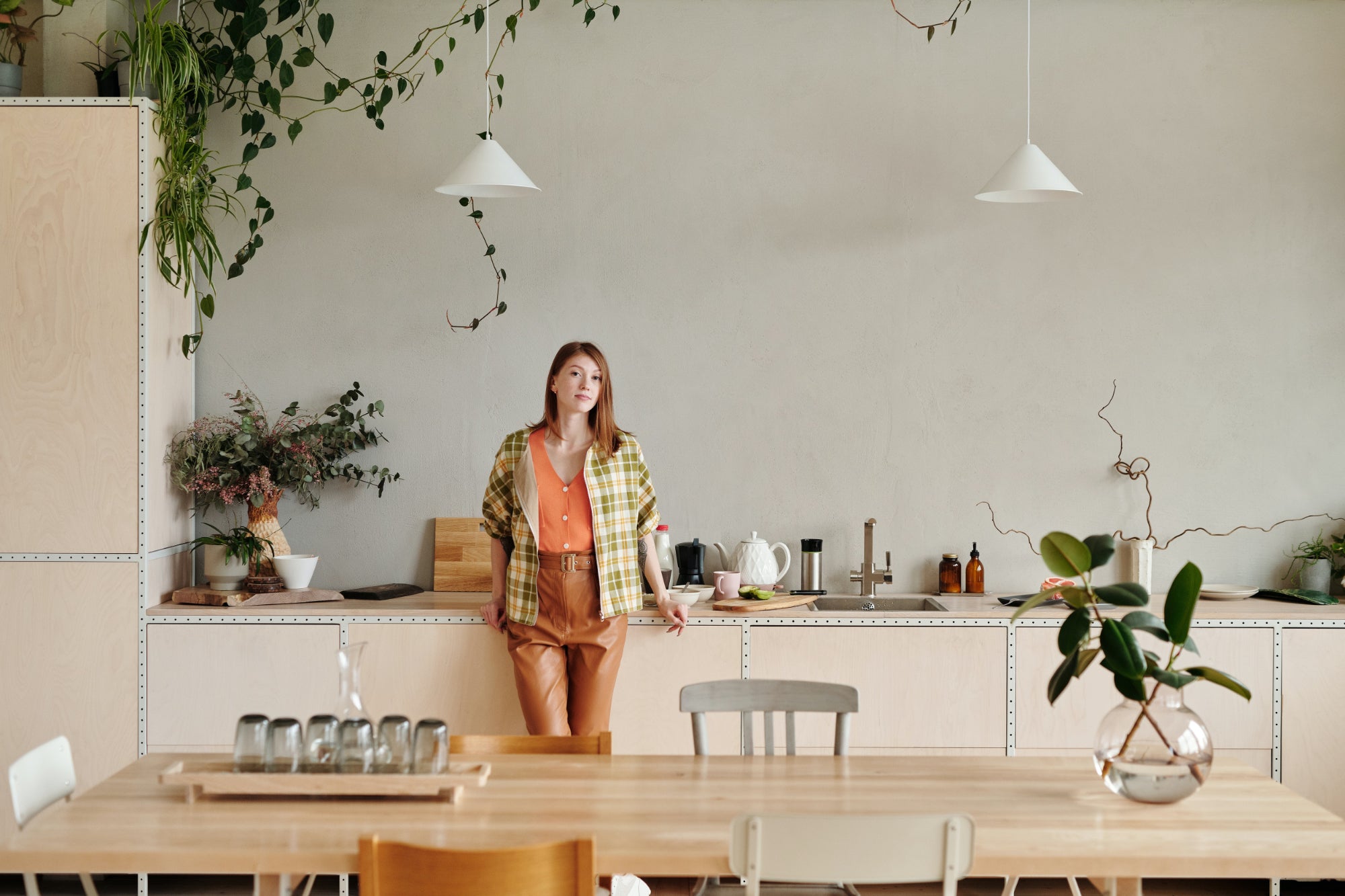 A person stands in a large neutral modern kitchen full of plants